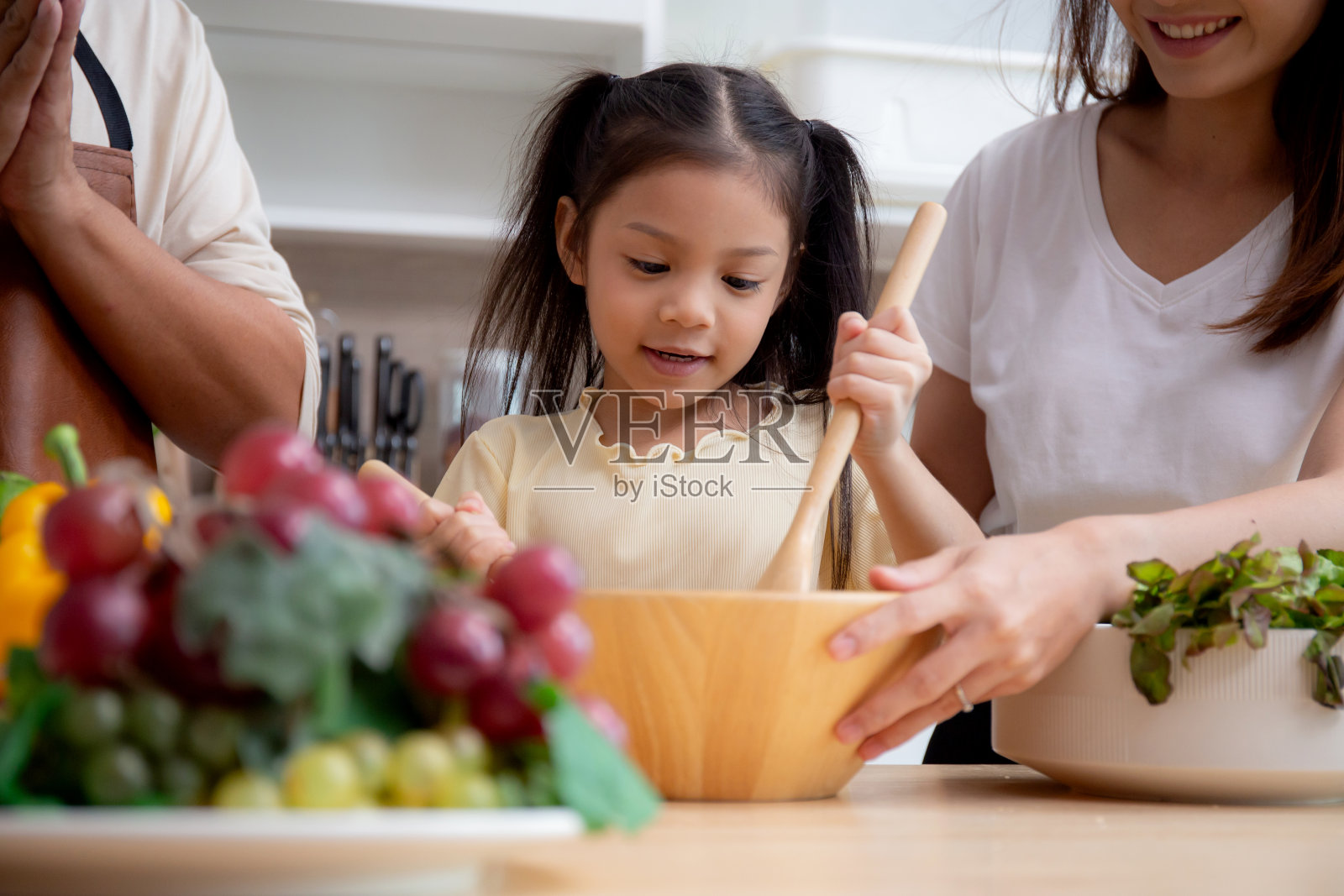 幸福的亚洲家庭与父亲，母亲和女儿在家里的厨房一起准备烹饪沙拉蔬菜食品，快乐的爸爸，妈妈和孩子用沙拉做早餐，生活方式的概念。照片摄影图片