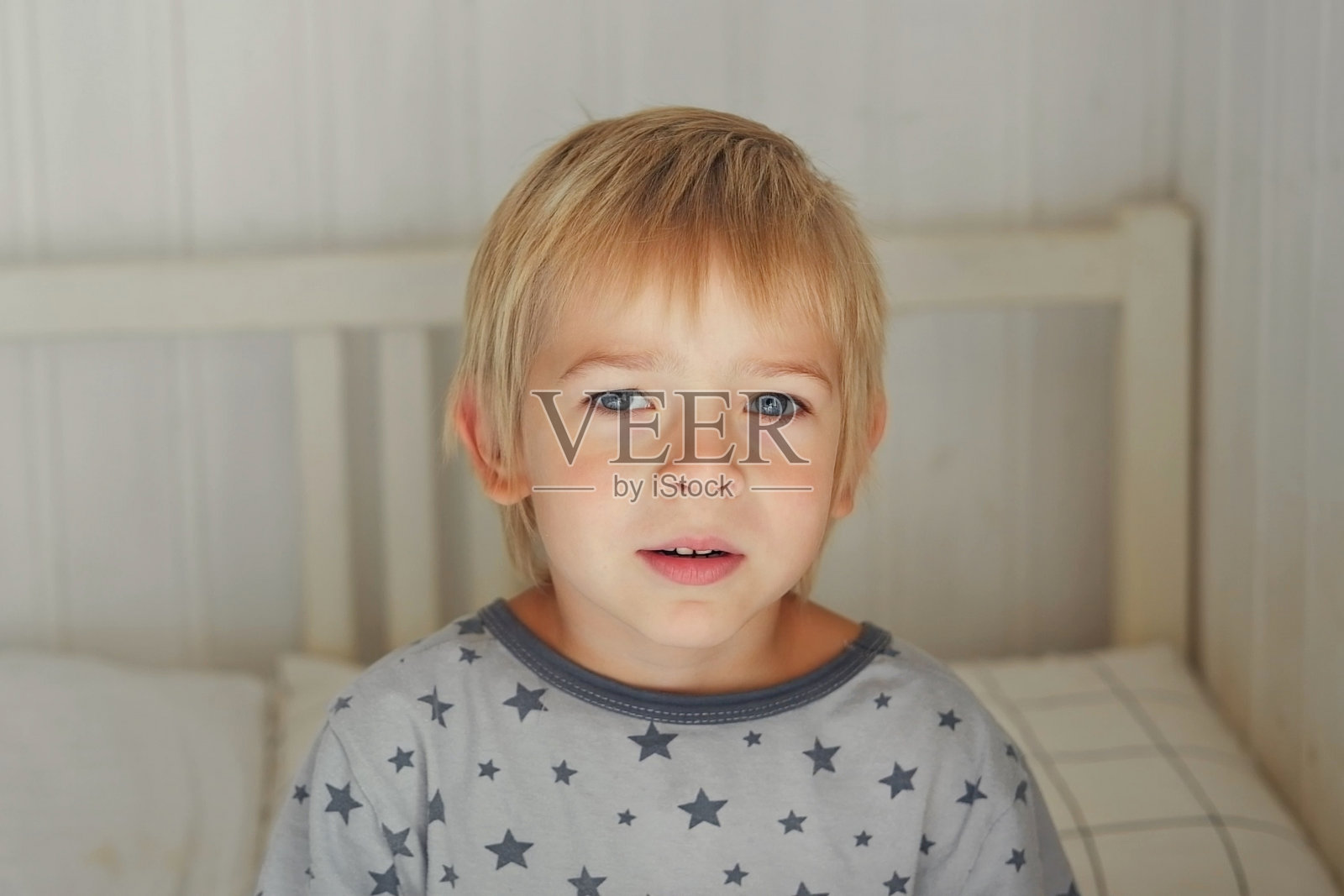 5岁男孩穿着睡衣在明亮的卧室里的肖像。孩子做鬼脸。小男孩躺在白床上的滑稽可笑的肖像。可爱的白人小孩看着镜头不想睡觉照片摄影图片