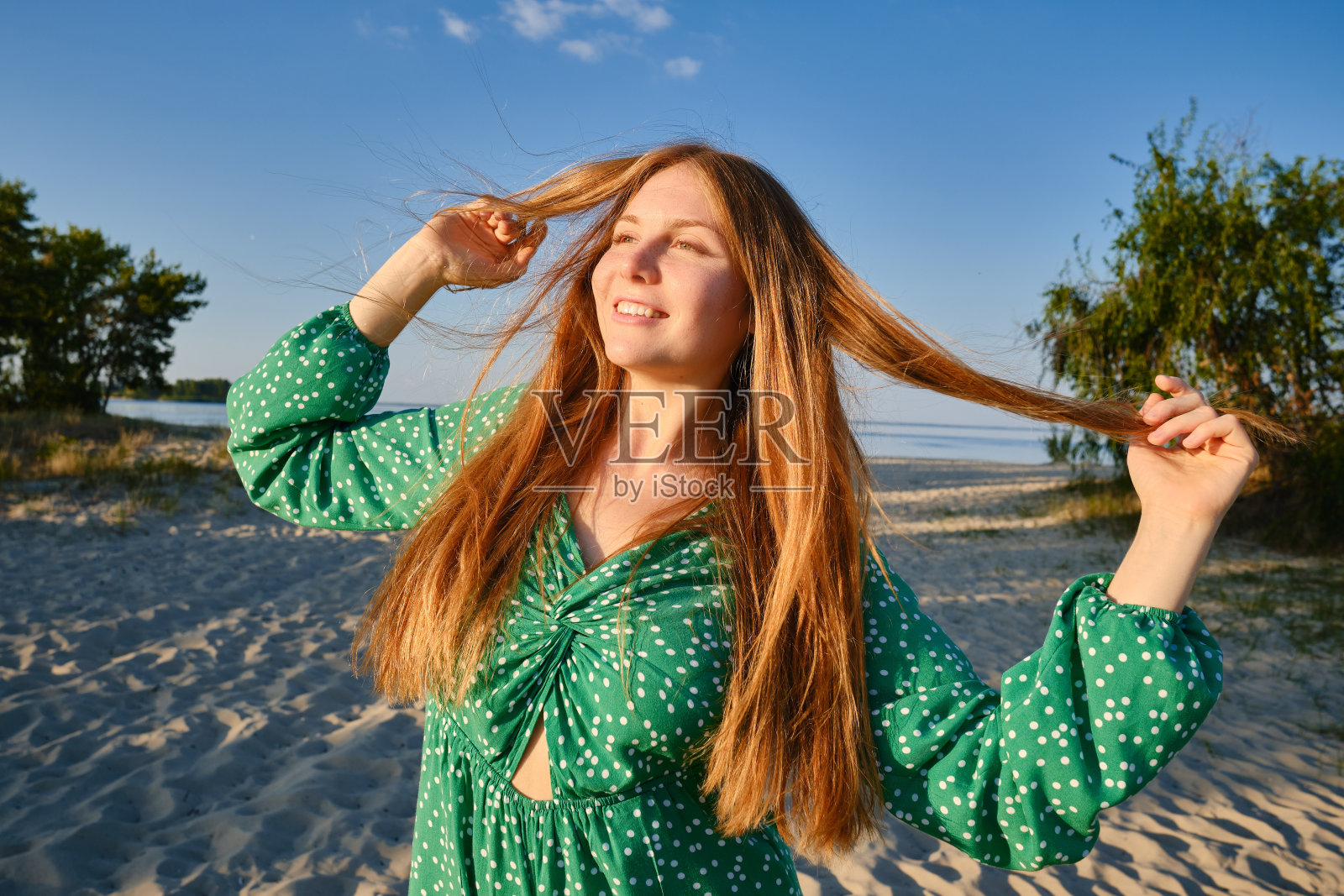 一个美丽的微笑的女孩在日落时的肖像。快乐开朗的红头发女孩在海滩上笑照片摄影图片