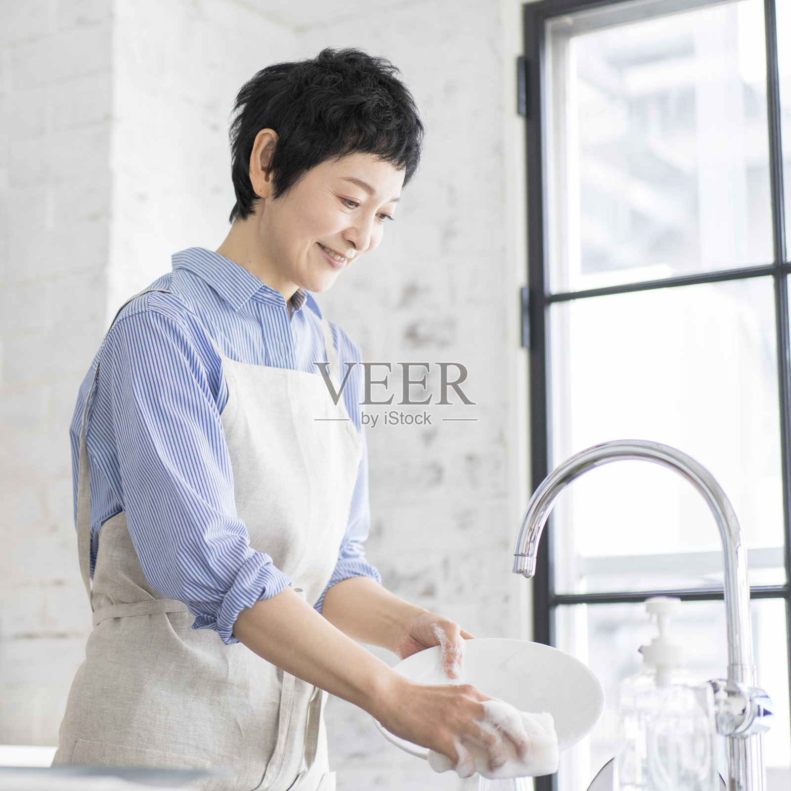 一个亚洲妇女正在厨房洗盘子。照片摄影图片