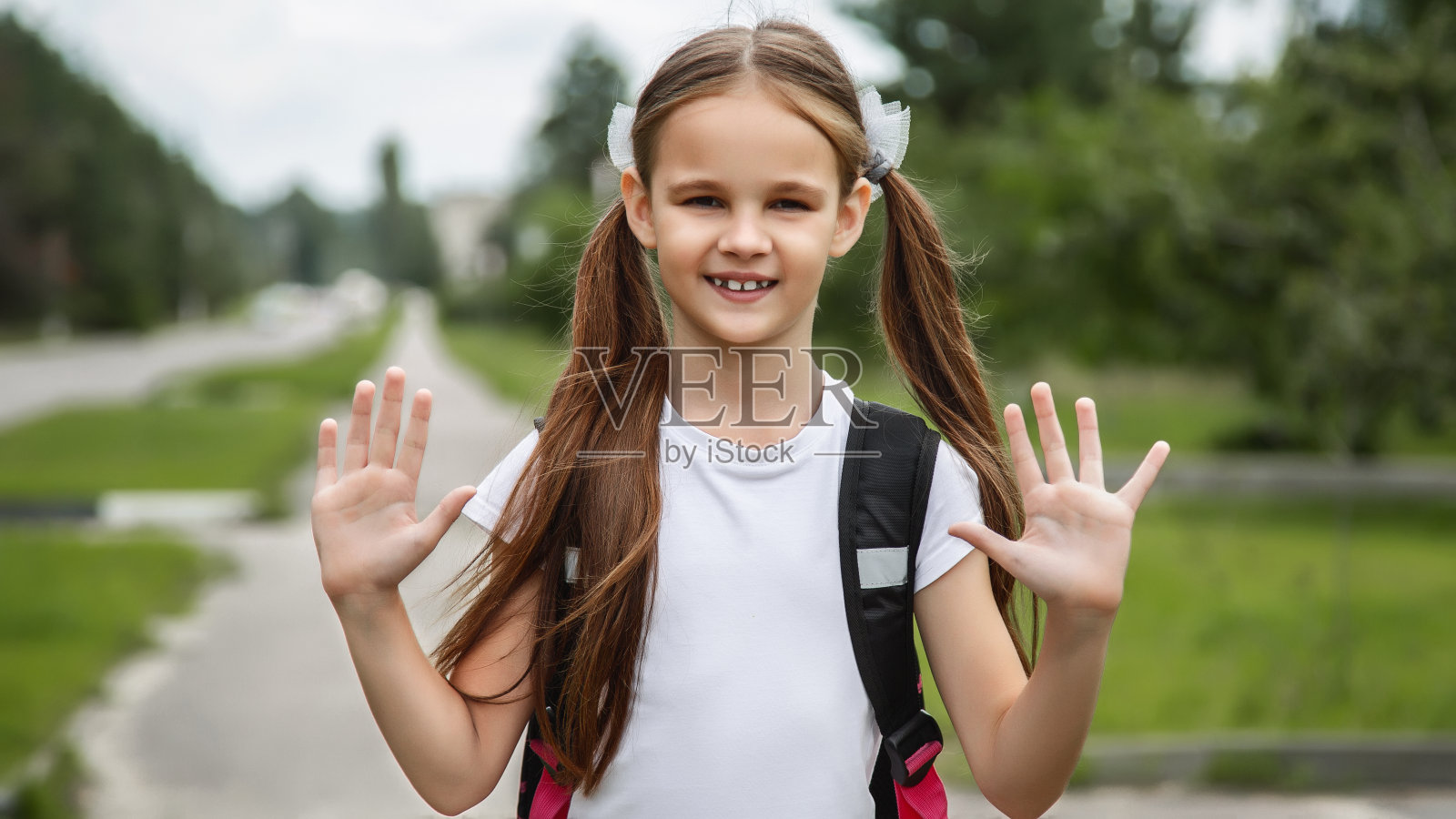 带着书包站在户外的快乐女孩的肖像。小女生开心上学，回学校，教育理念。可爱的女学生微笑着看着镜头照片摄影图片
