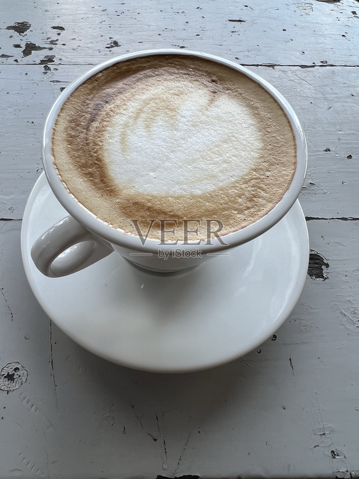 在木制背景上，白色杯子里有心形图案的咖啡。照片摄影图片