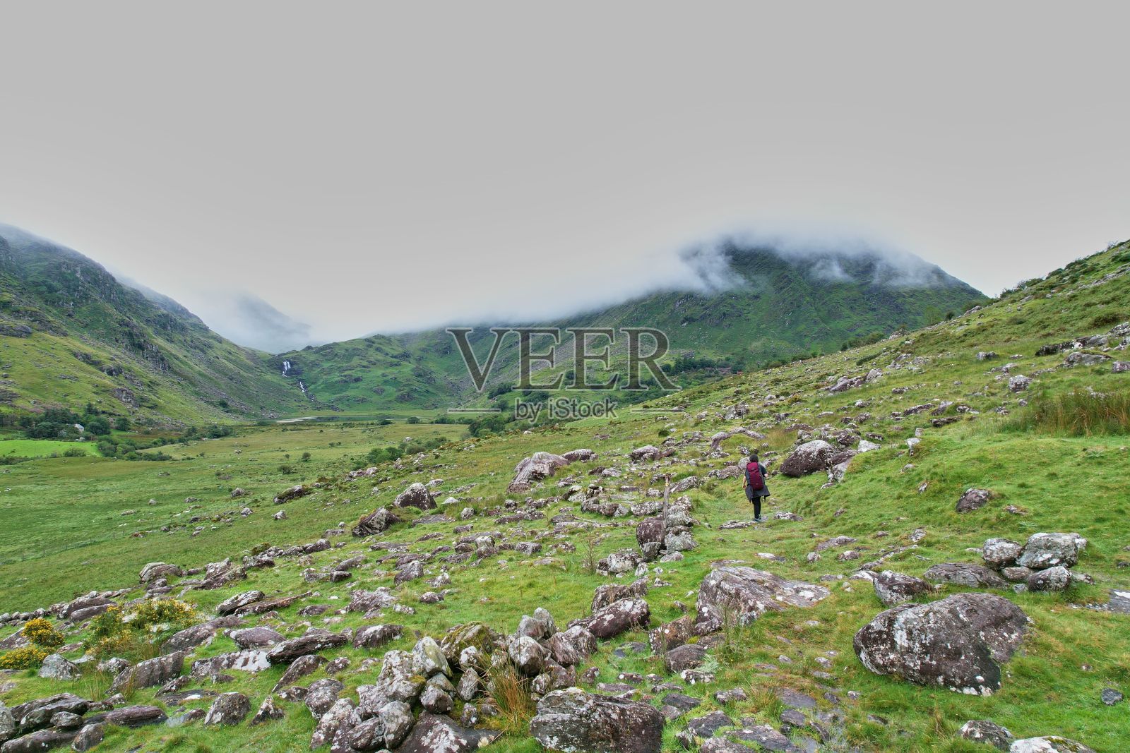 孤独的身影出现在广阔的山间草地上，穿过爱尔兰郁郁葱葱的绿草地照片摄影图片