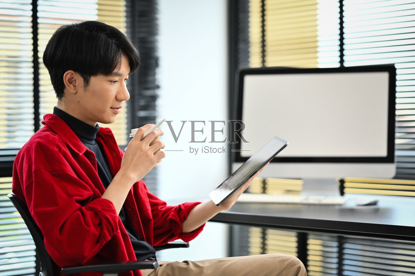 近景现代商人拿着纸杯，在办公桌上使用数码平板电脑照片摄影图片