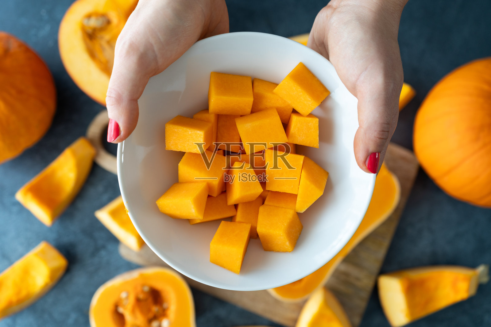 拿着南瓜丁的女人。准备应季的秋季食物。照片摄影图片