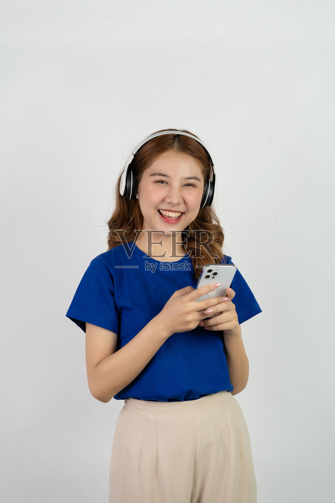 相当快乐的亚洲少女使用手机播放音乐从智能手机应用程序，快乐的微笑，同时听流媒体音乐在白色背景，科技概念照片摄影图片