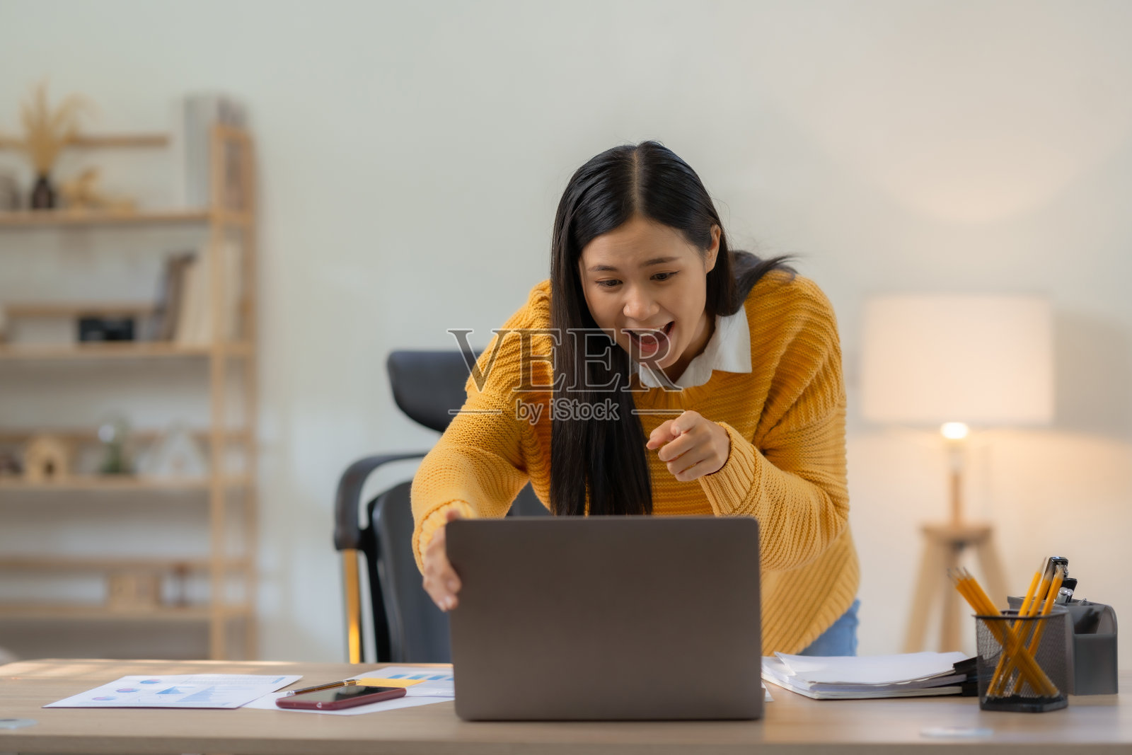 快乐的年轻亚洲女性举起胜利的手，在家里用笔记本电脑开心地微笑。成功，胜利，胜利，胜利，祝贺，概念。照片摄影图片
