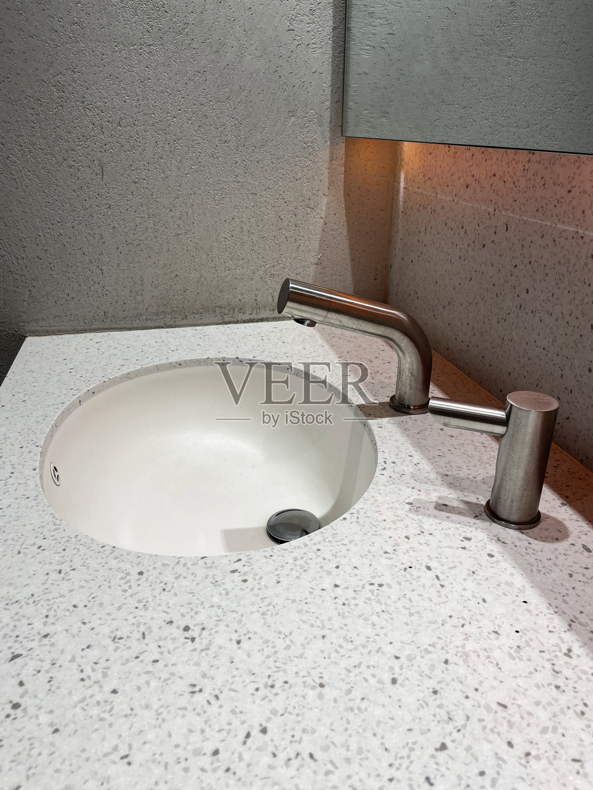 白色陶瓷水槽嵌入斑点图像，水磨石柜台在公共厕所，铬，红外运动传感器水龙头，墙镜，铬皂分配器，高架视图，重点在前景照片摄影图片