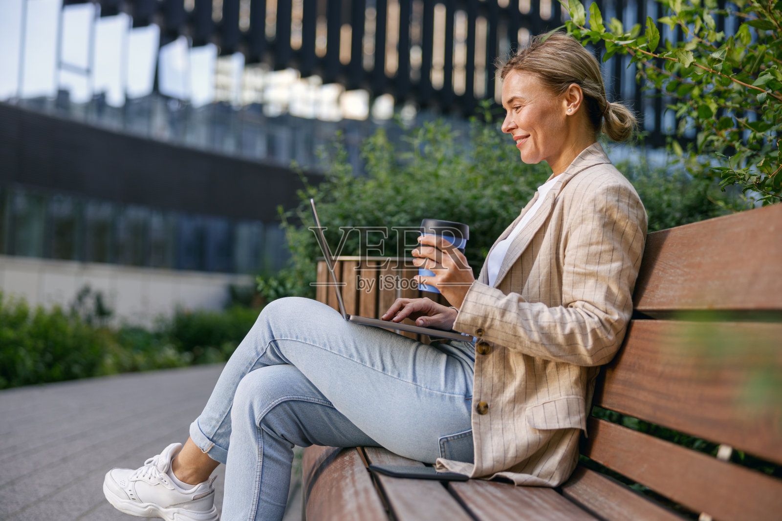 微笑的女商人在办公室外喝着咖啡，用笔记本电脑工作。远程工作概念照片摄影图片