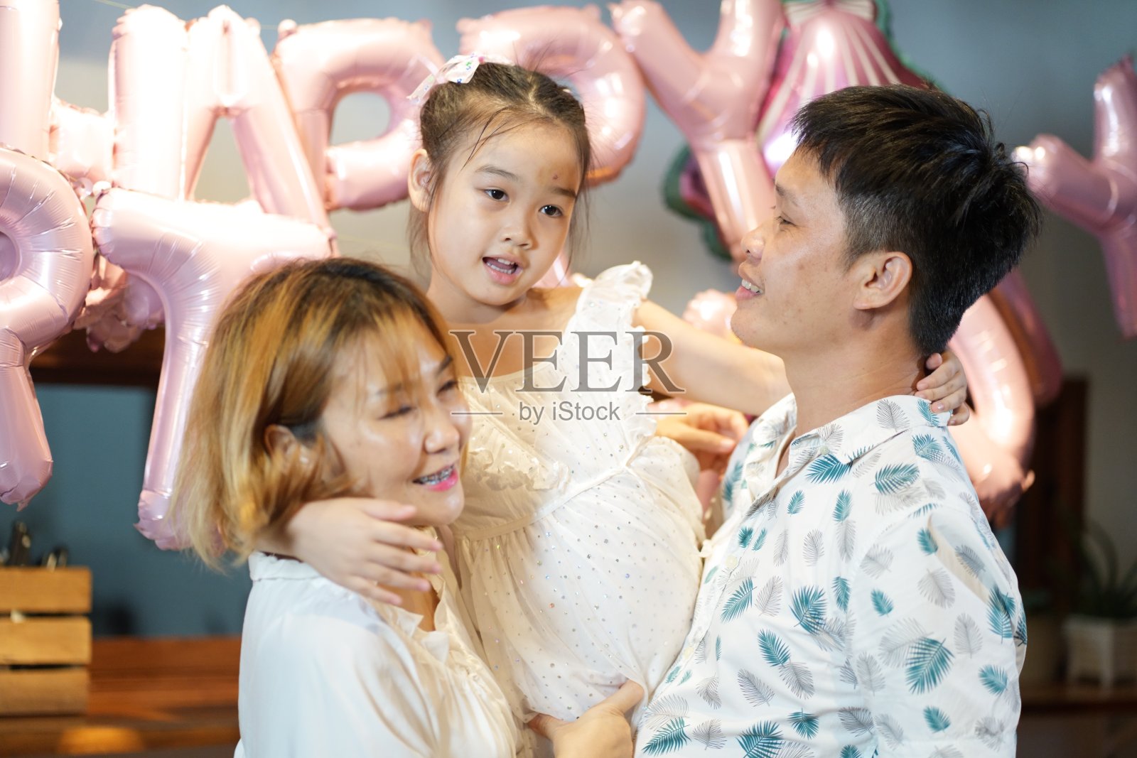 在女儿的生日聚会上，欢快的爸爸和妈妈幸福地拥抱着他们的女儿照片摄影图片