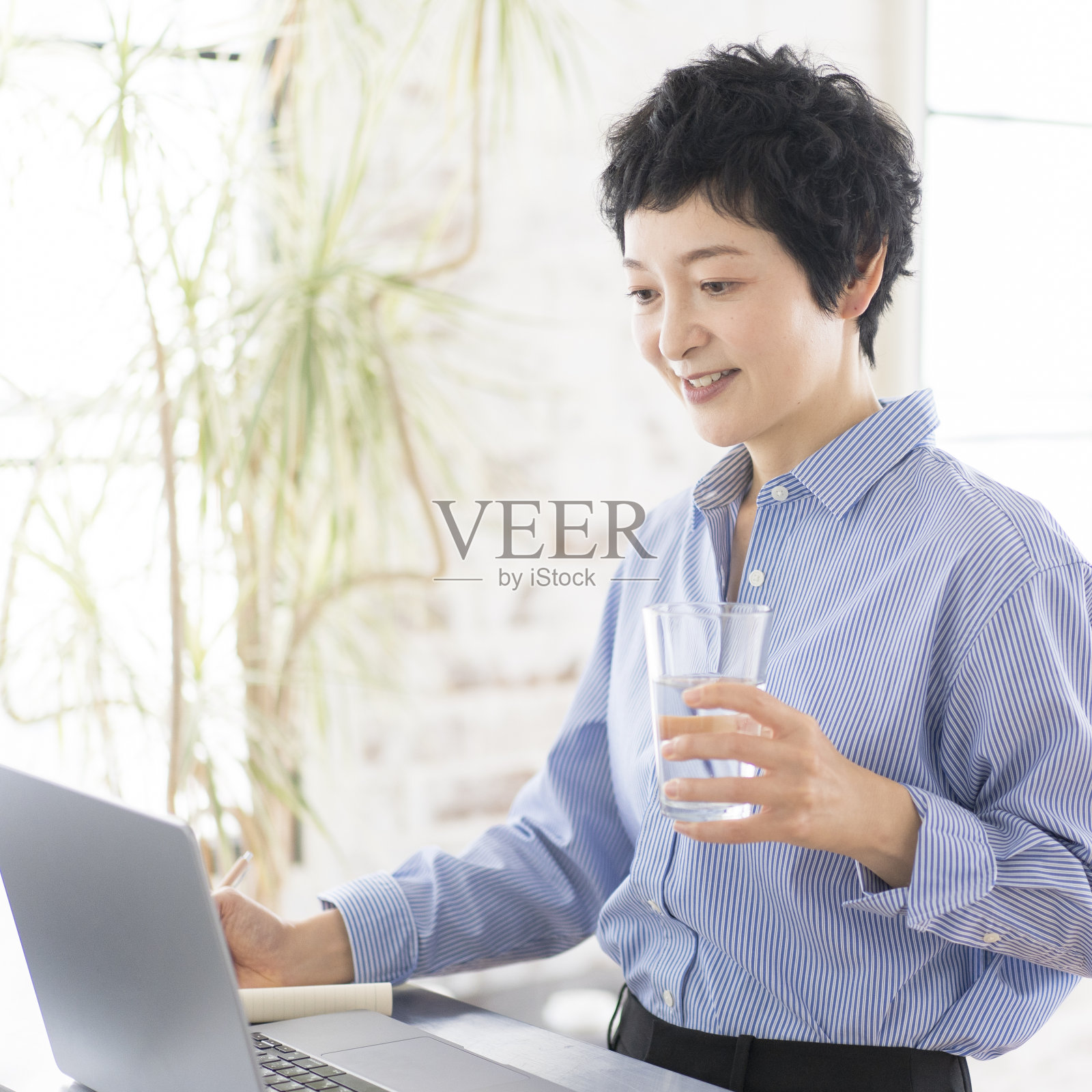 一个女人正站着用笔记本电脑工作。照片摄影图片