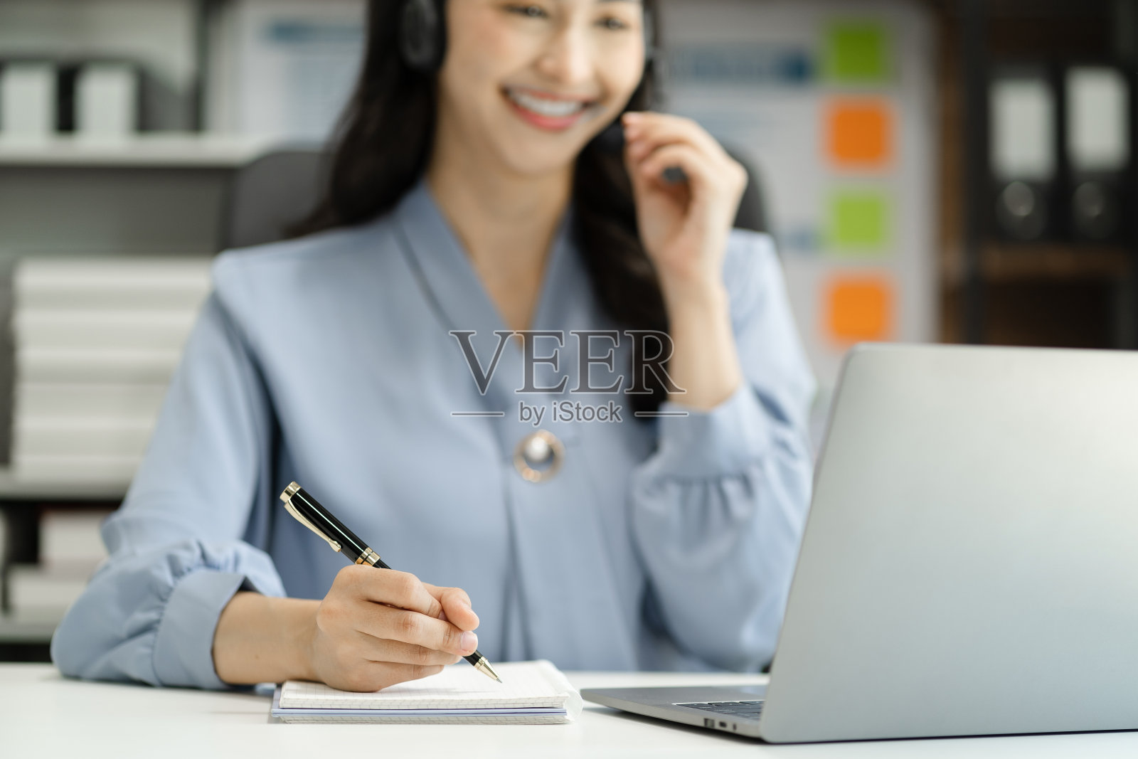 严肃的呼叫中心接线员戴着无线耳机与客户交谈，戴着耳机的女士带着麦克风在客户支持中心的电话中咨询客户，看着电脑屏幕。照片摄影图片