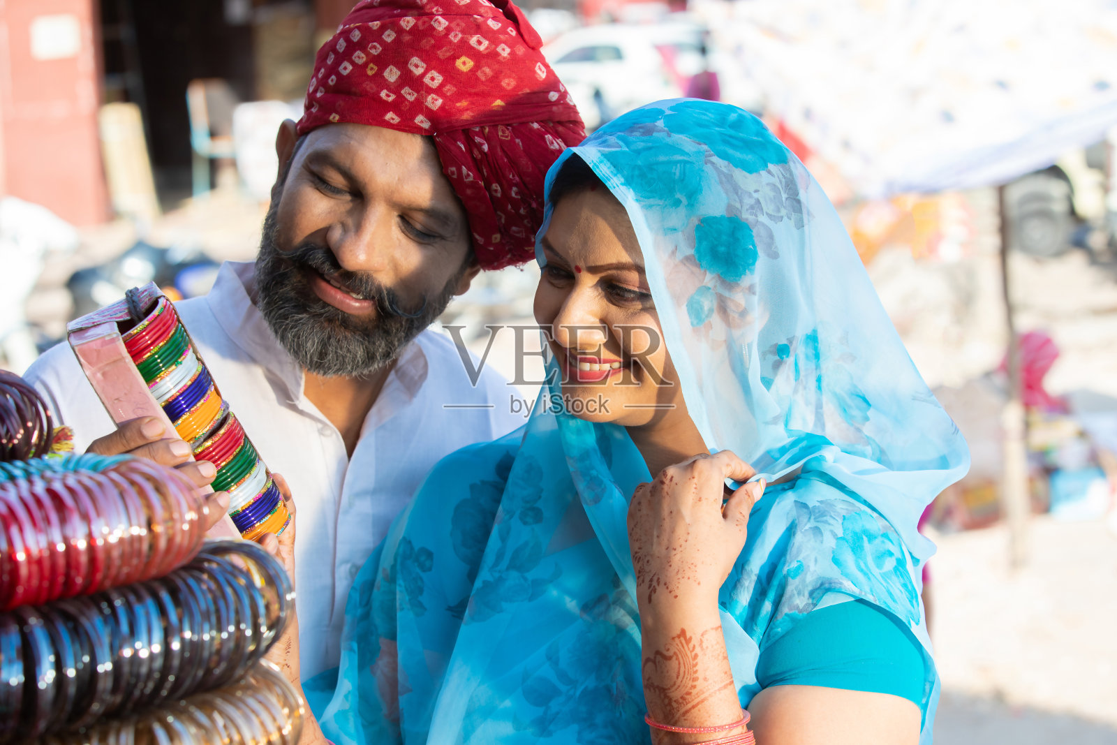 幸福的传统印度夫妇在当地的街头市场购物的特写，男人戴着红头巾，女人穿着纱丽从商店购买彩色手镯。照片摄影图片