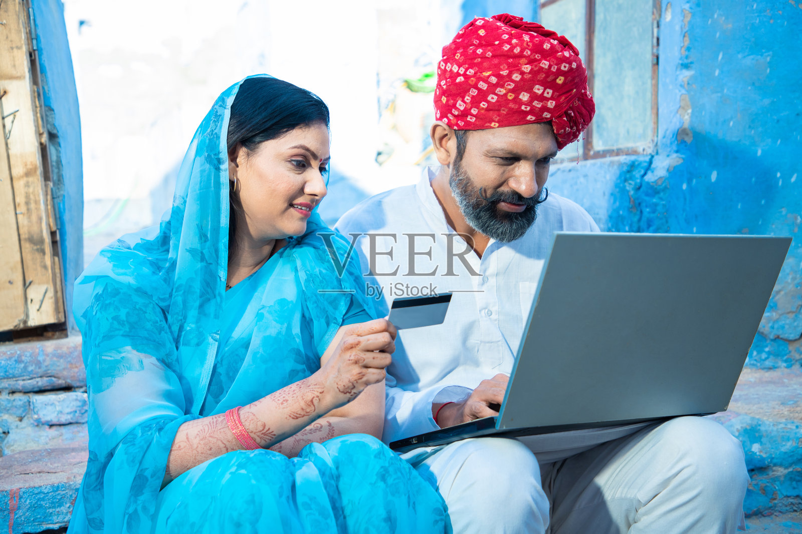传统的印度夫妇用笔记本电脑拿着银行卡进行网上支付，女人穿着纱丽拿着借记卡，男人戴着头巾看着电脑屏幕网上银行照片摄影图片