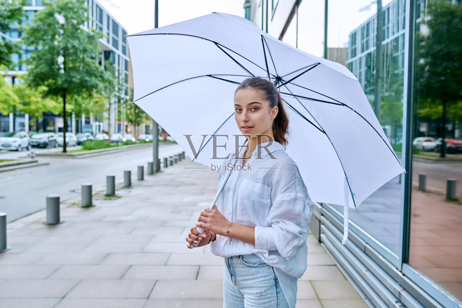 夏日阴天，年轻的少女在城市街道上的白色雨伞下照片摄影图片
