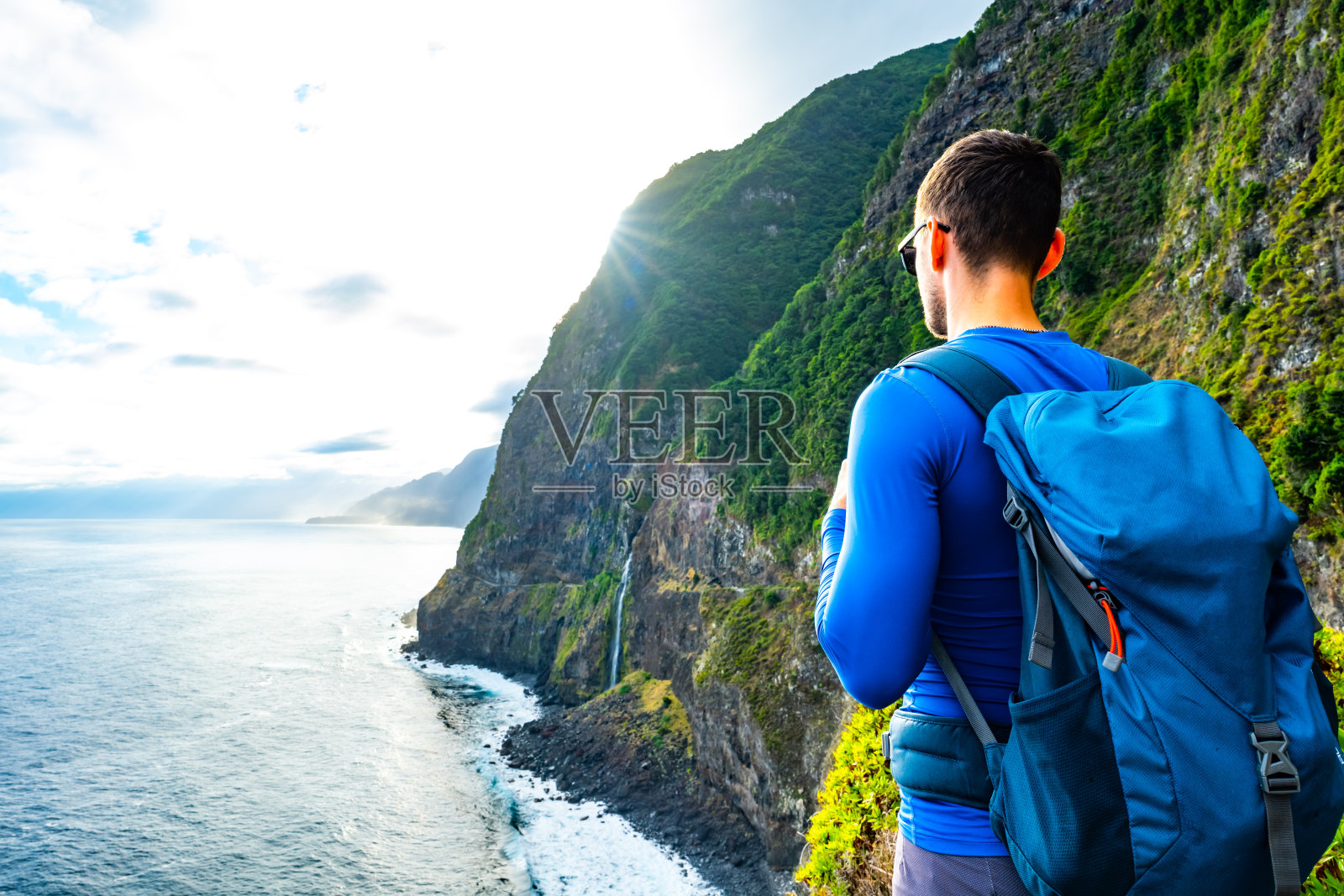 爱运动的男子在大气的早晨看着流入大海的瀑布。欧洲葡萄牙马德拉岛的新瓦村。照片摄影图片