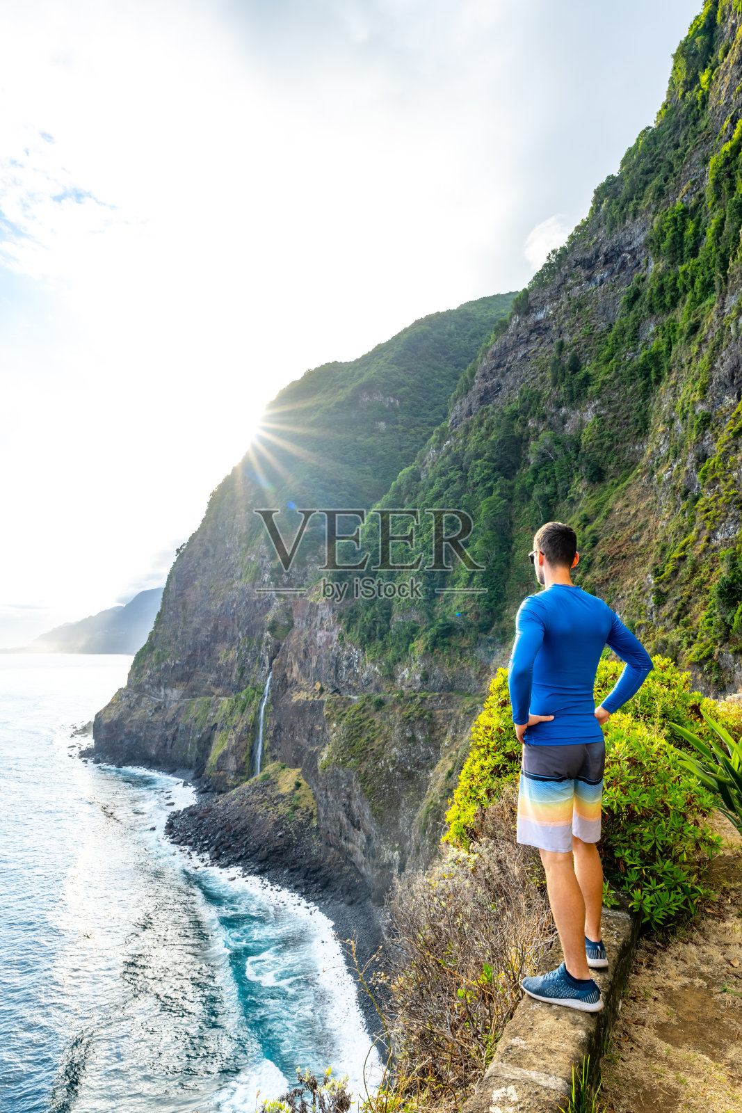 爱运动的男子在大气的早晨看着流入大海的瀑布。欧洲葡萄牙马德拉岛的新瓦村。照片摄影图片