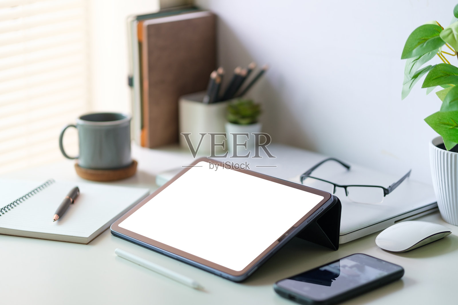 现代工作空间，白色办公桌上有平板电脑、盆栽植物、笔记本和咖啡杯。空白屏幕显示器的图形显示蒙太奇。照片摄影图片