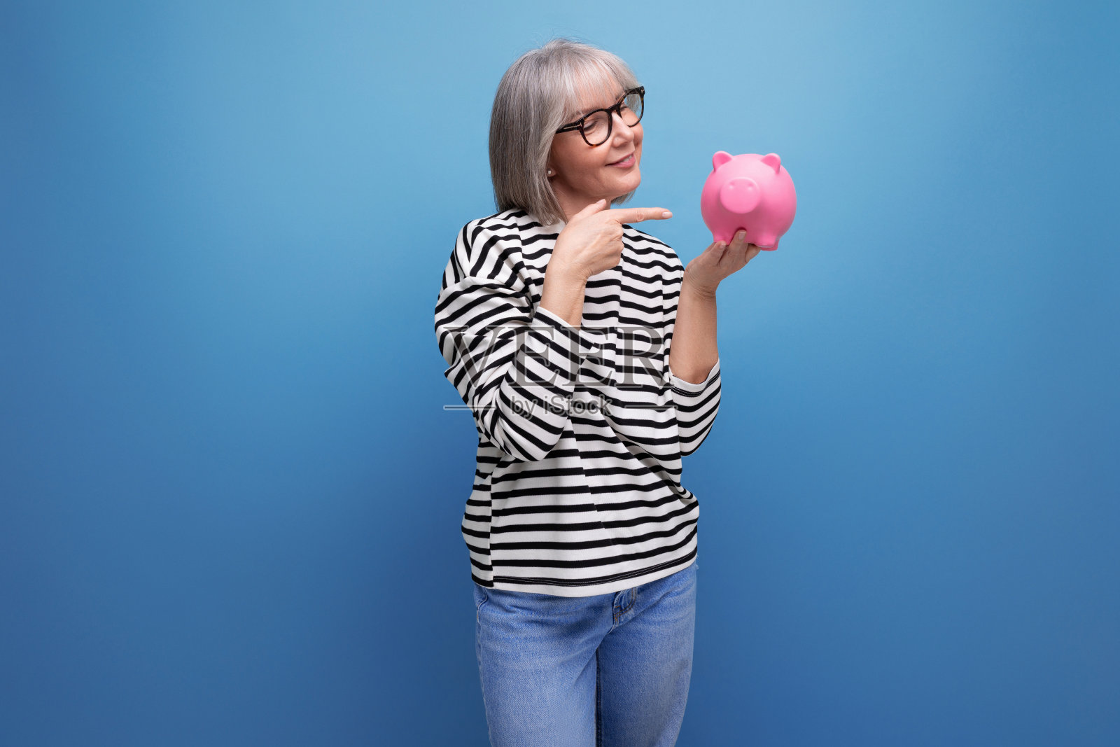 可爱的中年妇女拿着一个装满钱的储蓄罐，背景明亮，有复制空间照片摄影图片