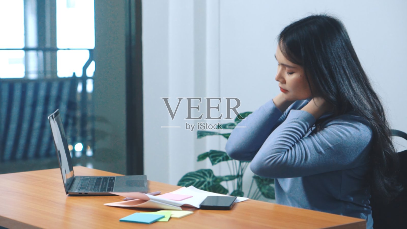 亚洲年轻女性，坐在办公桌前上网销售时颈部疼痛。照片摄影图片