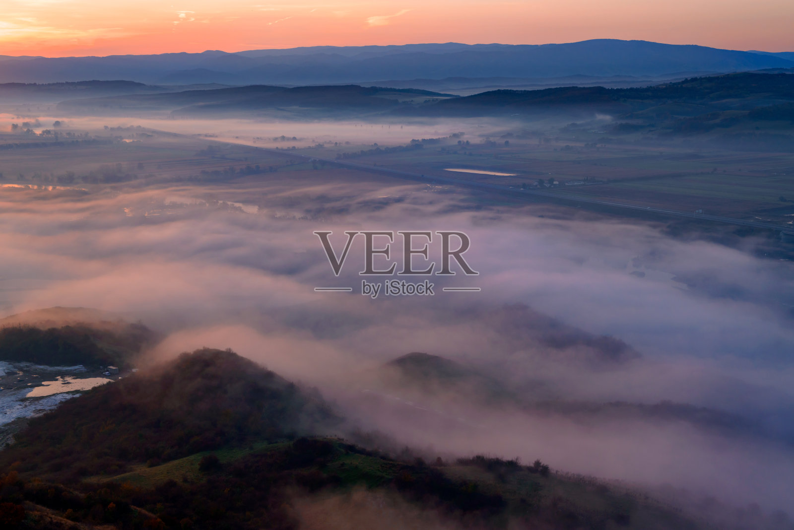 鸟瞰清晨薄雾中的山谷，美丽的高地。低低的云和雾笼罩着沉睡的草地。黎明时分，高山山谷薄雾缭绕。宁静的乡村时光照片摄影图片