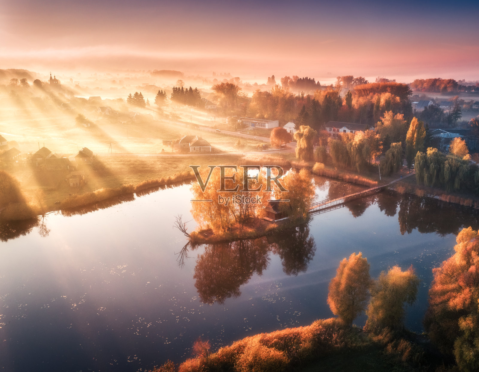 鸟瞰图的房子与五颜六色的树木在小岛上的湖。秋天有雾的日出。美丽的风景有雾中的村庄，金色的阳光，在水中的倒影。乌克兰沦陷。俯视图照片摄影图片