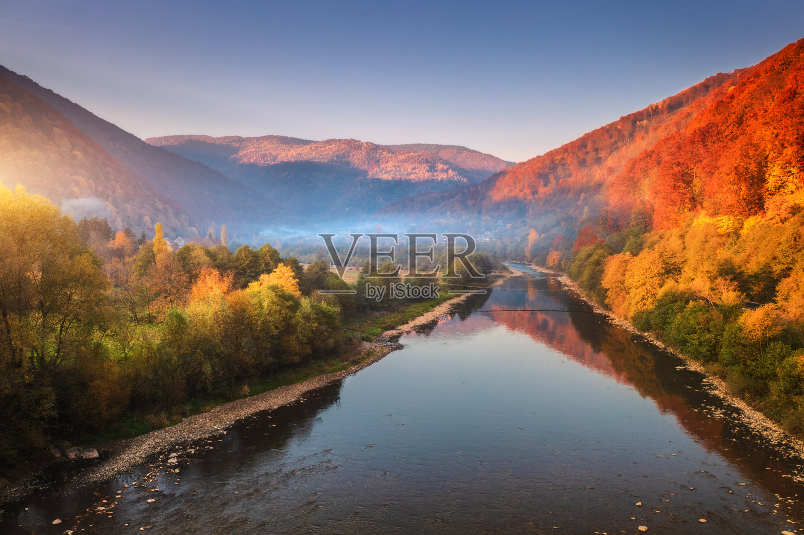 鸟瞰图，在秋天日落时，蓝色的湖在山上，红色和橙色的森林在雾中。乌克兰喀尔巴阡山脉的河流。农村景观。山丘和树林的俯视图。旅行照片摄影图片