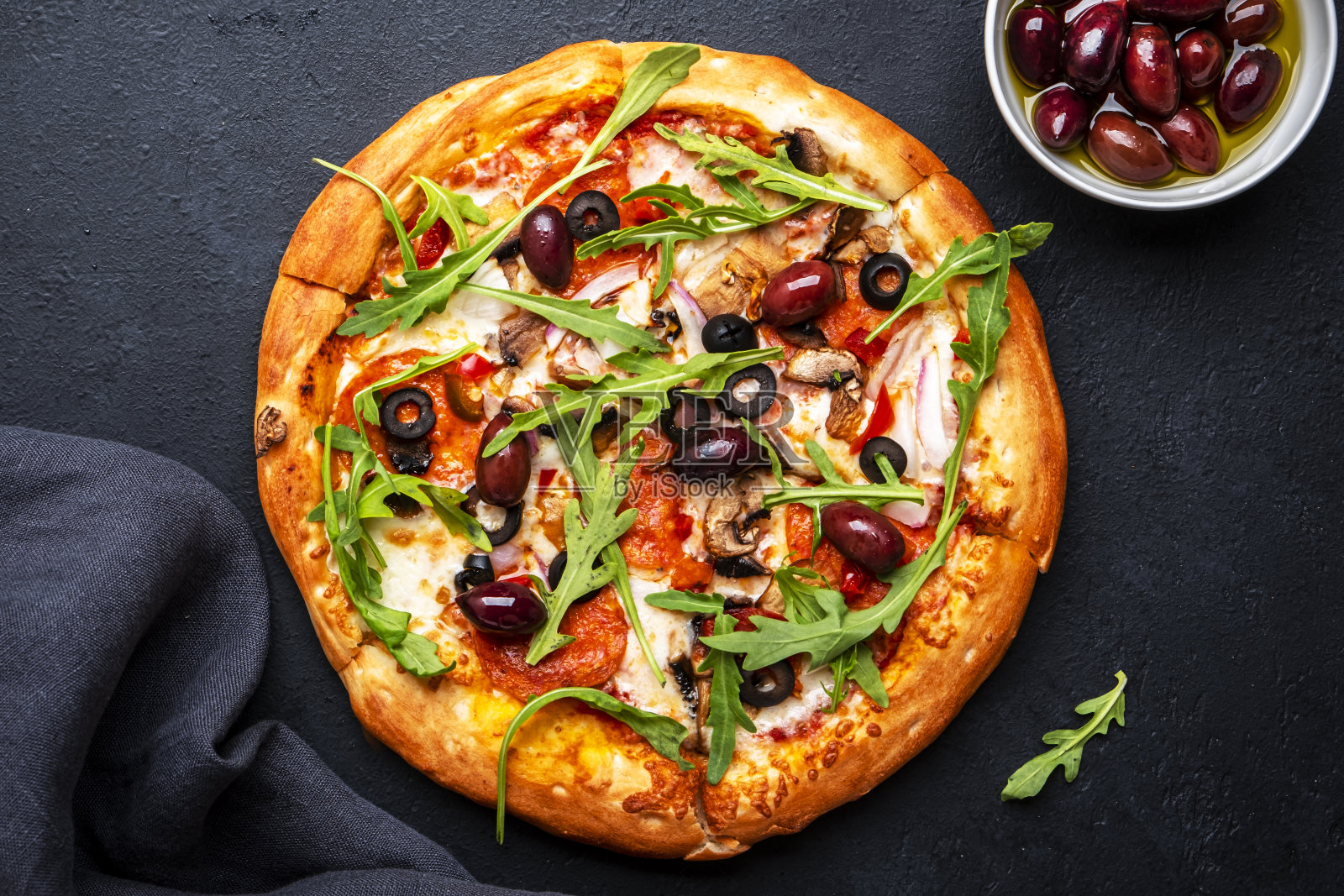 自制披萨配意大利腊肠、芝士、蘑菇、黑橄榄、番茄酱和芝麻菜，黑色桌面背景，俯视图照片摄影图片