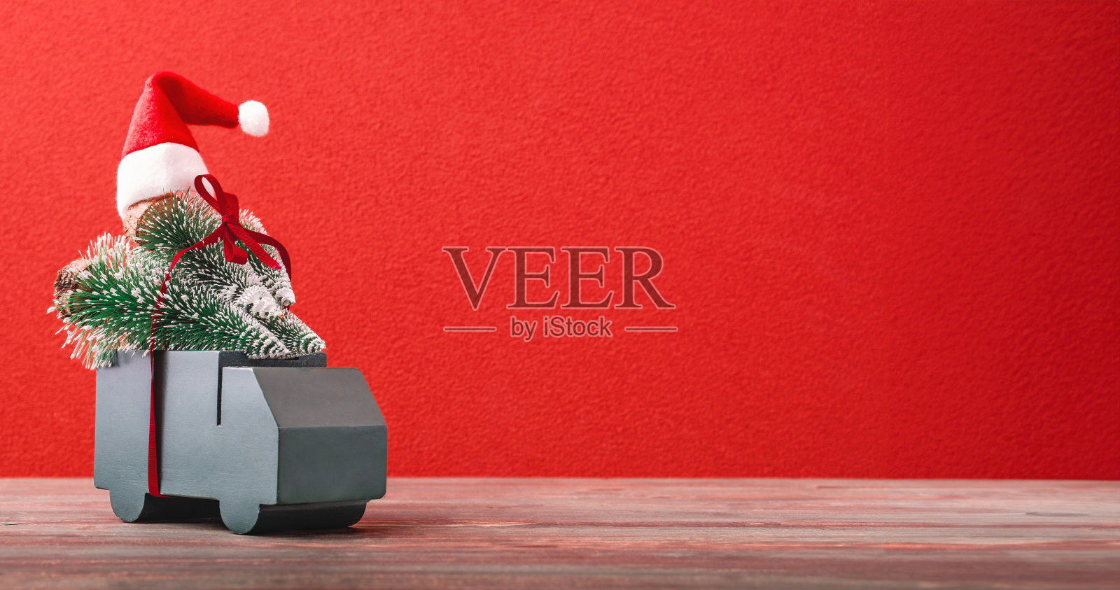 圣诞贺卡。绿色汽车载着松树和礼物缎带在红色背景的桌子上照片摄影图片
