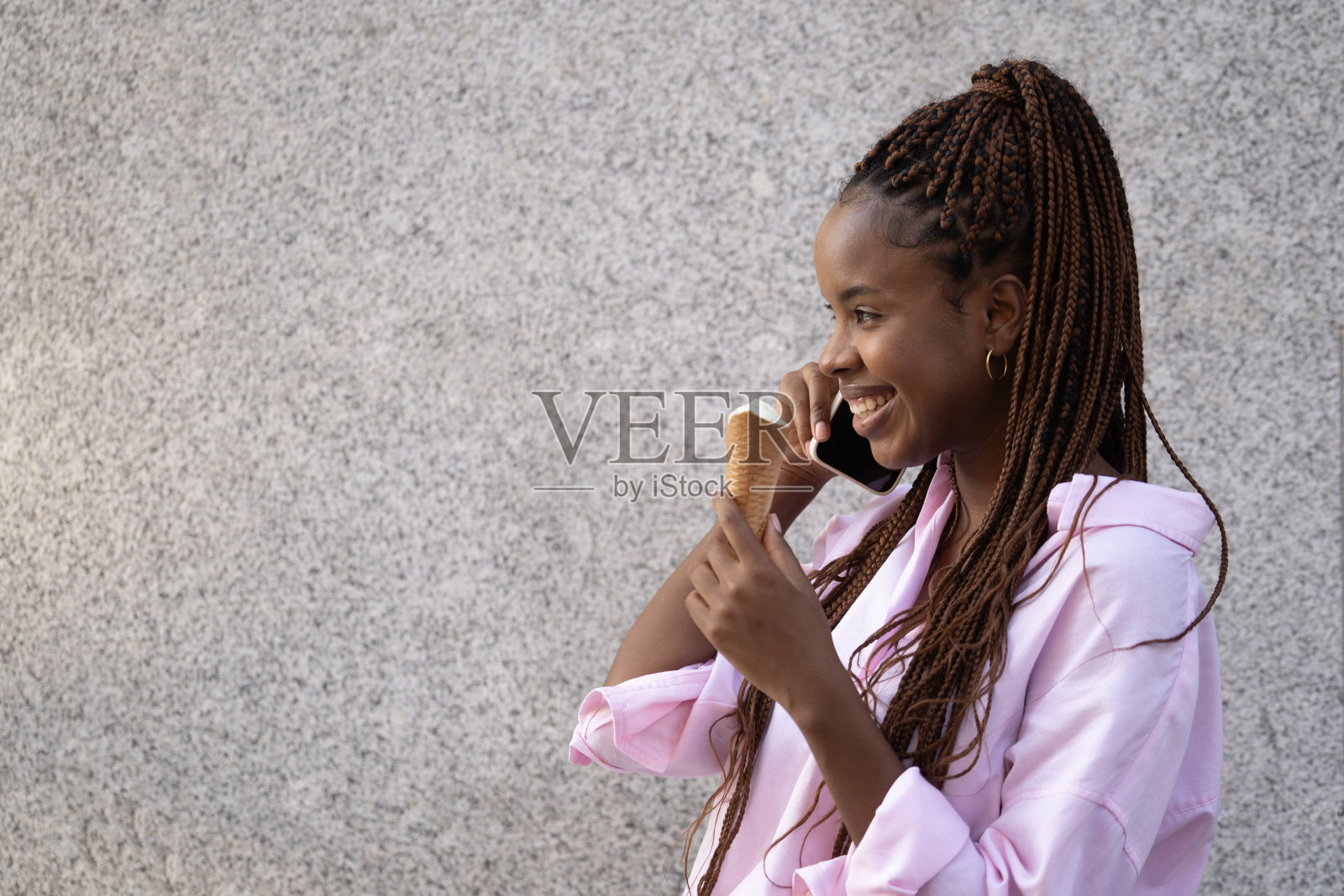 一个快乐的美国黑人女孩一边吃冰淇淋一边打电话。灰色背景隔离照片摄影图片