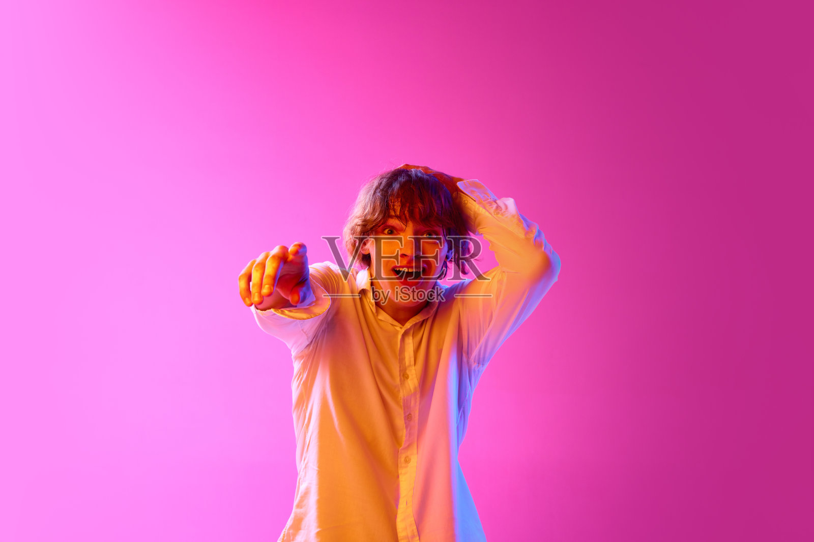 年轻兴奋的小伙子用手指着，在霓虹灯下粉红色的工作室背景下表达情感。销售照片摄影图片