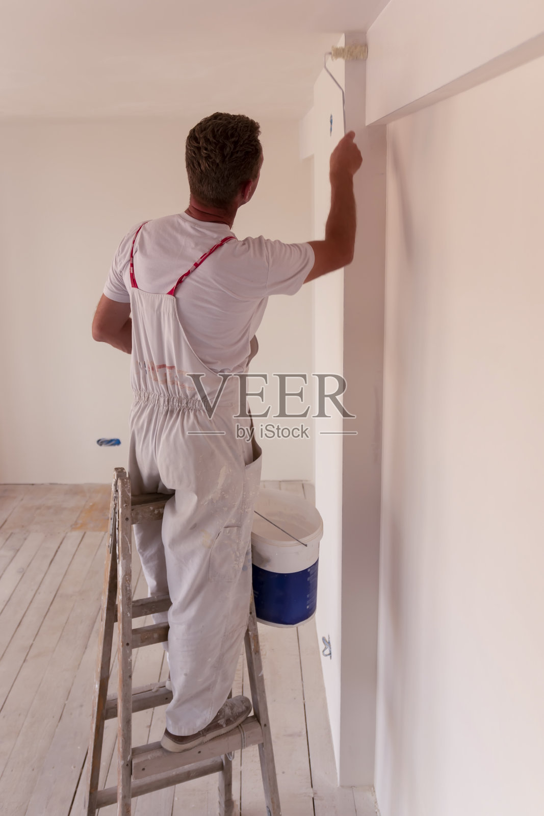 一个人在空房间里用油漆滚筒粉刷白色的墙壁和天花板照片摄影图片