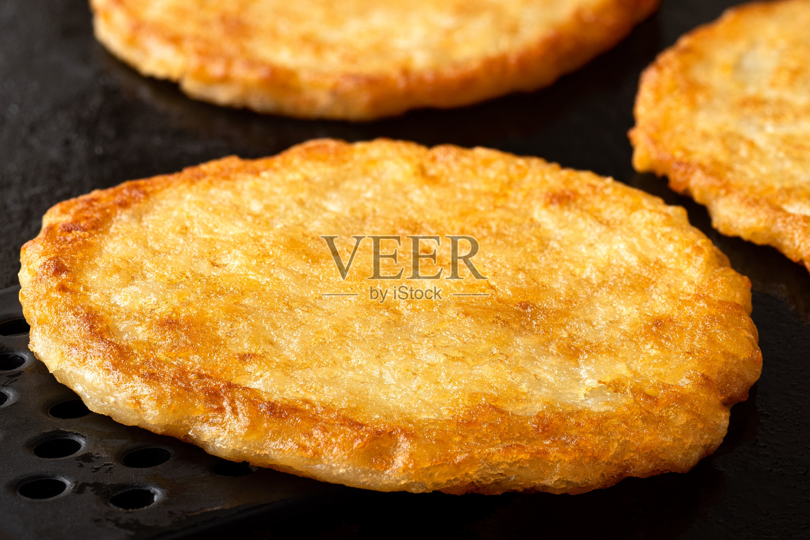 马铃薯煎饼的细节在铸铁煎锅与黑色刮刀。照片摄影图片