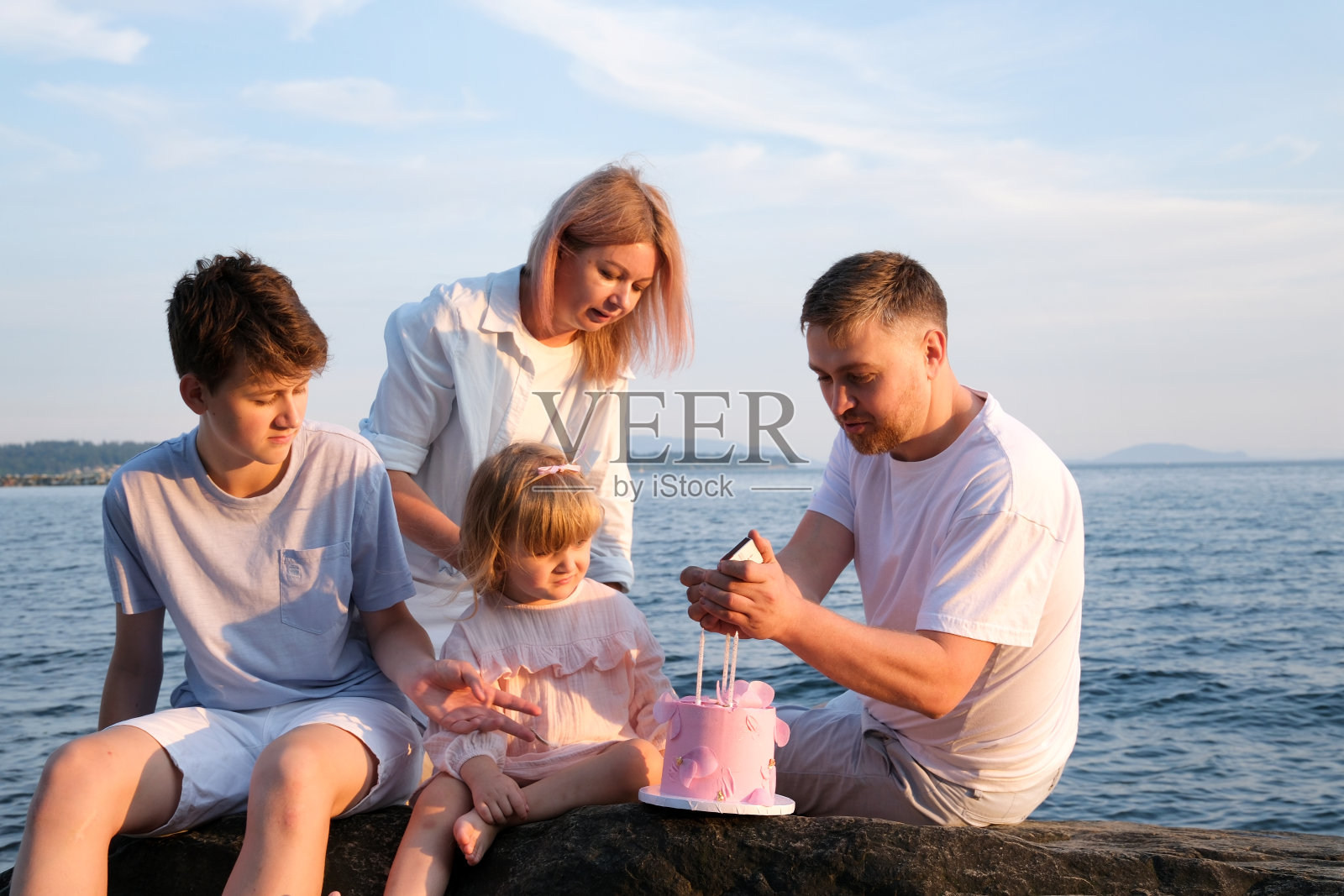幸福的家庭在海边庆祝小女孩的生日妈妈带来了一个装有蛋糕的盒子女孩打开礼物爸爸妈妈哥哥姐姐在海边一个阳光明媚的日子照片摄影图片