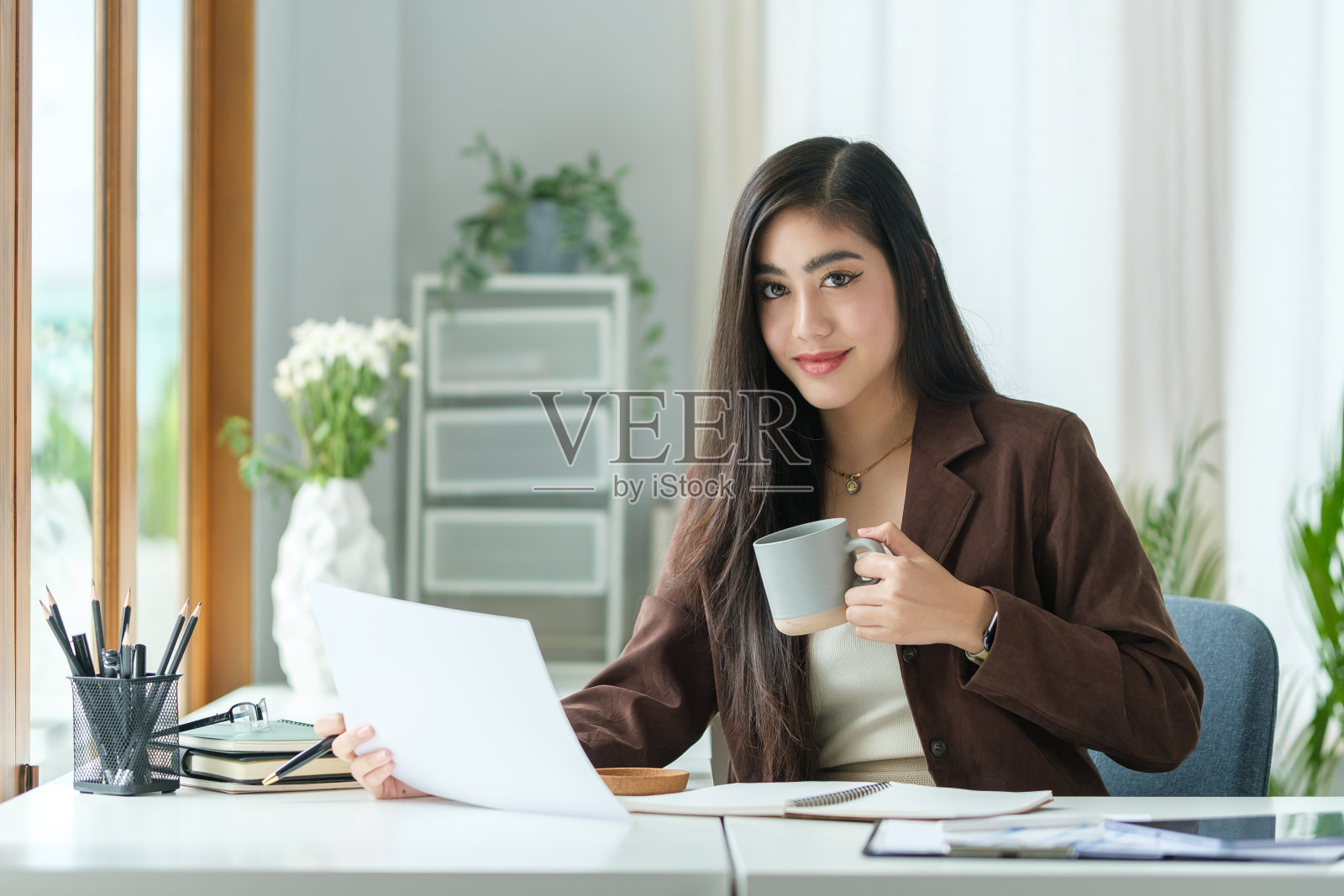 女商人坐在现代的工作场所，对着镜头微笑。照片摄影图片