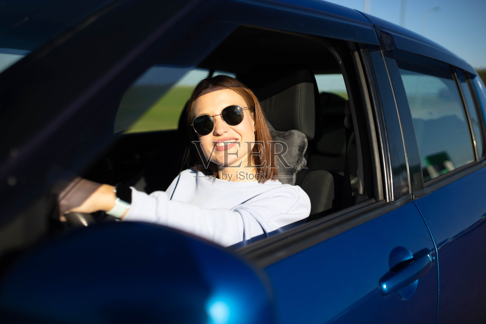 美丽的年轻女子在阳光明媚的日子里开着车微笑着。照片摄影图片