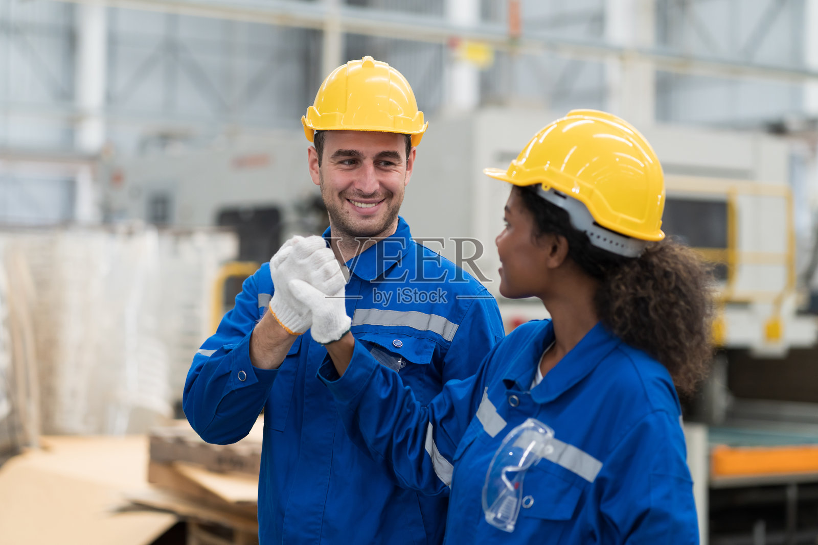 在工业工厂里，穿着安全制服，头戴安全帽，双臂交叉站立的男女工程师工人。一组工程师在工作场所。生产线工程师团队照片摄影图片