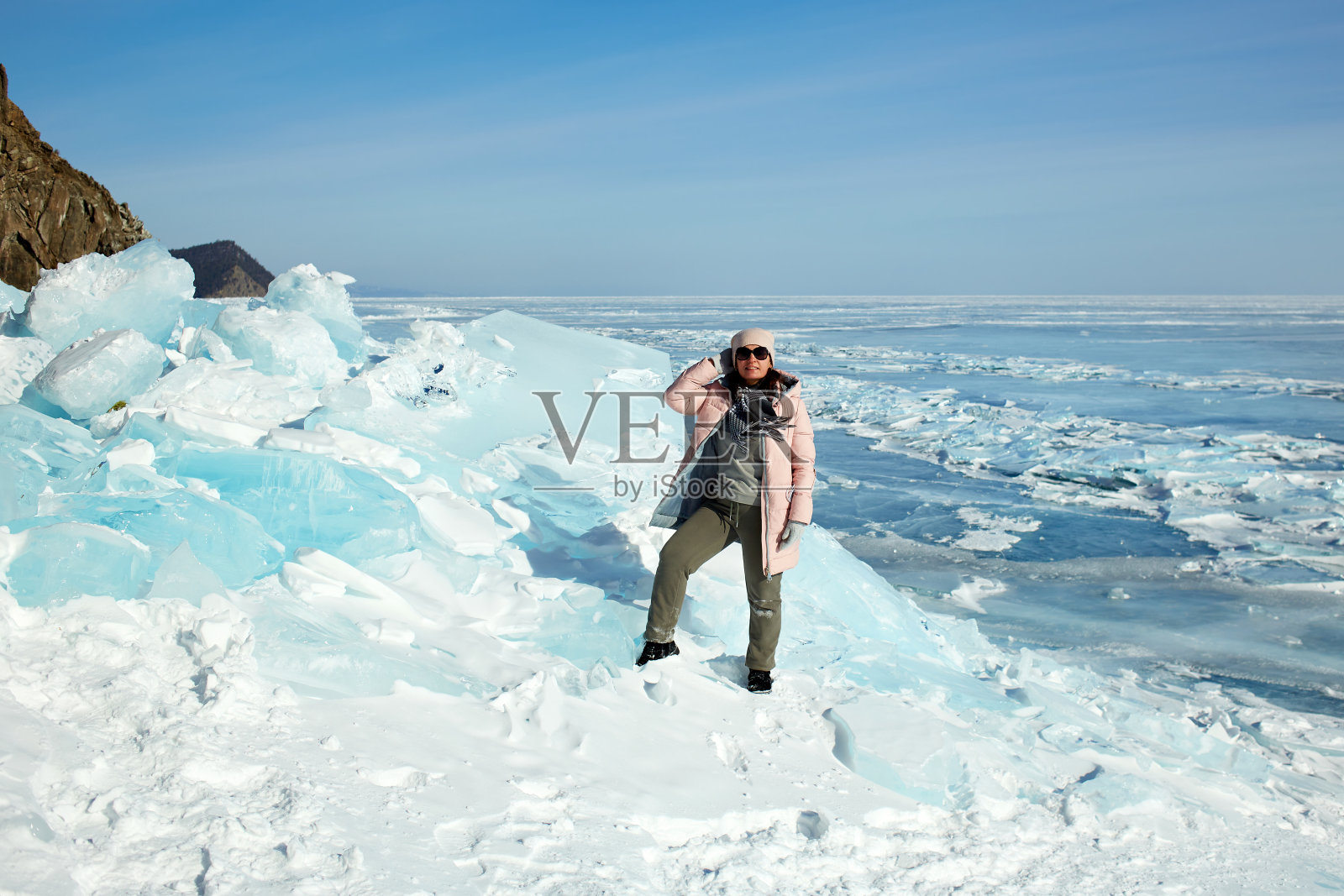 一位女性旅行者站在巨大的冰块前，冰封的贝加尔湖上的冰丘。照片摄影图片