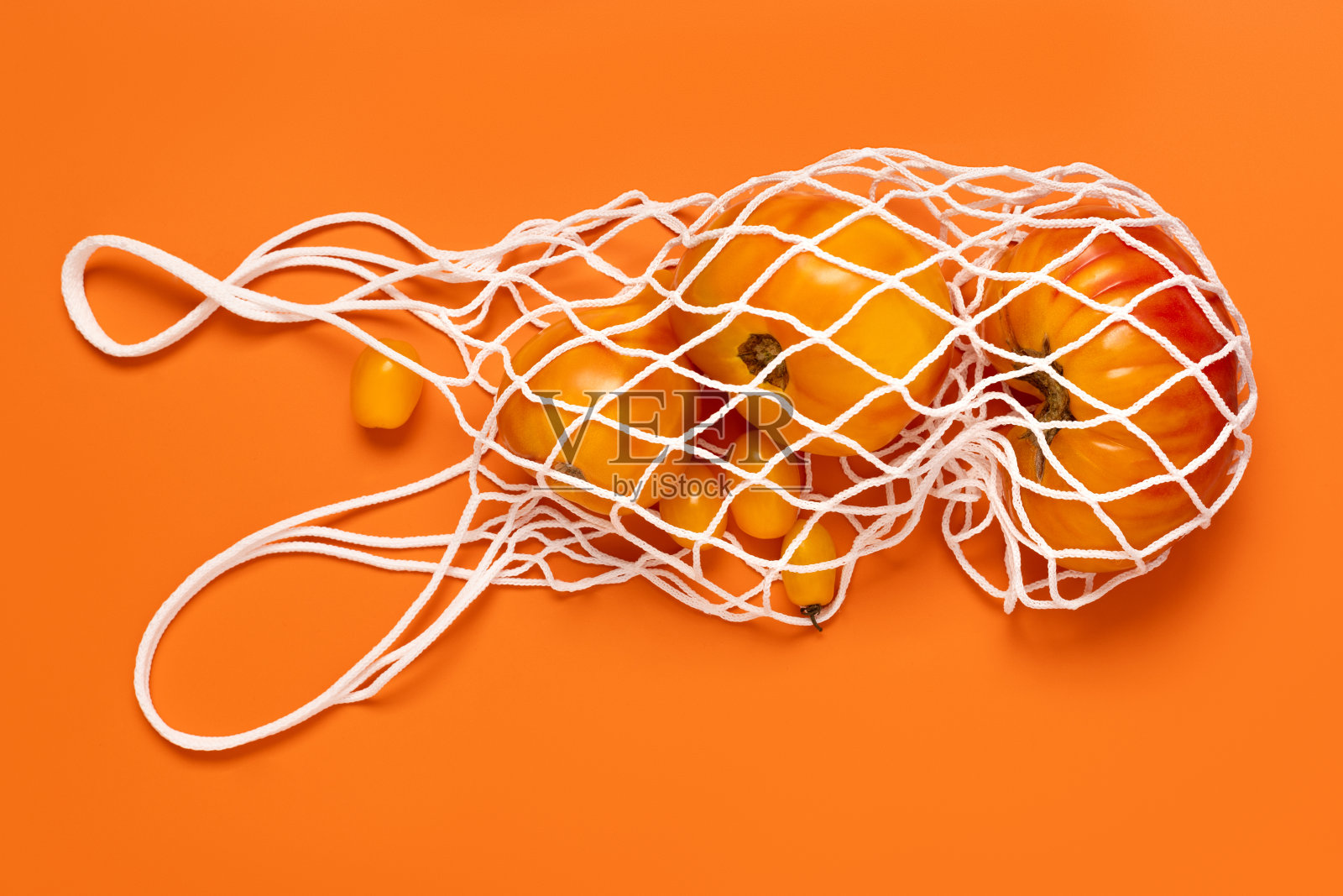 橙色背景上的白色网状购物袋里装着各色黄、黑、红西红柿，俯视图照片摄影图片
