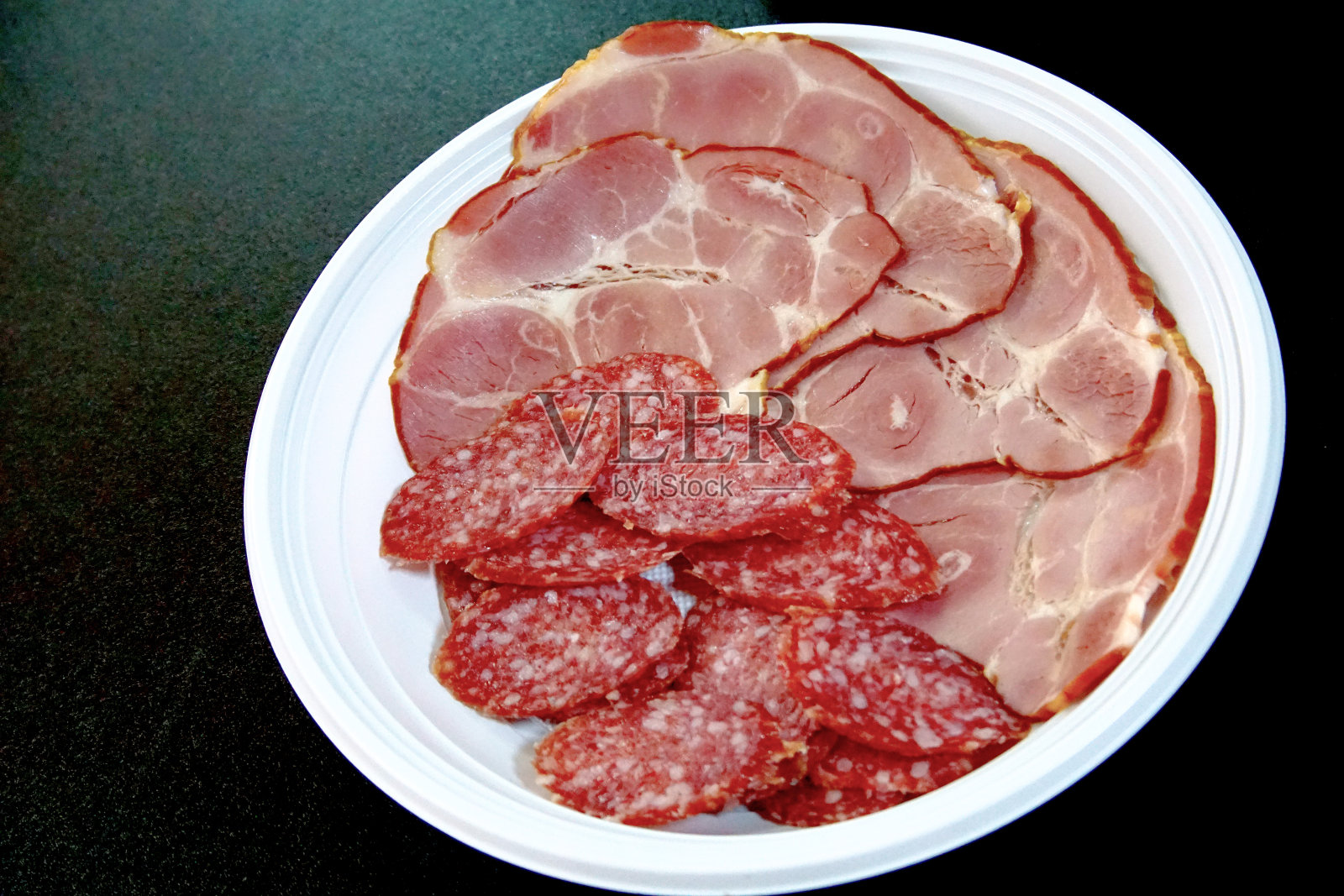 烟熏腊肠、意大利辣香肠和火腿片，用一次性塑料盘子盛着。照片摄影图片