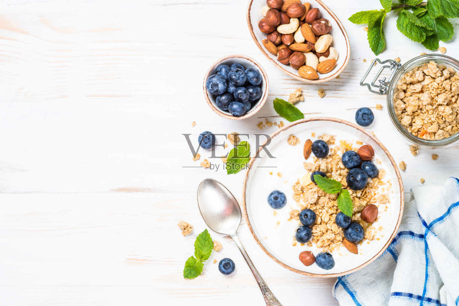 白色木桌上的酸奶格兰诺拉麦片配新鲜蓝莓。照片摄影图片