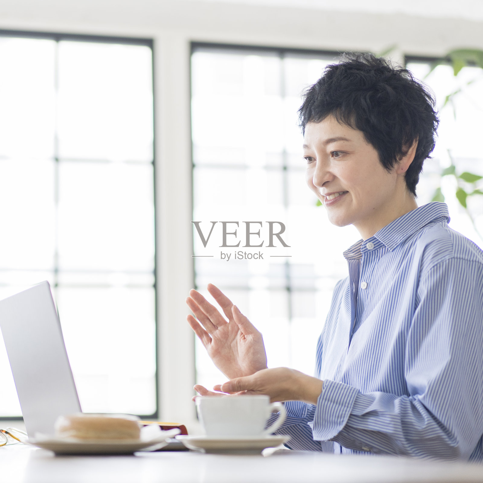 一位亚洲妇女一边说话一边看着笔记本电脑显示器。照片摄影图片