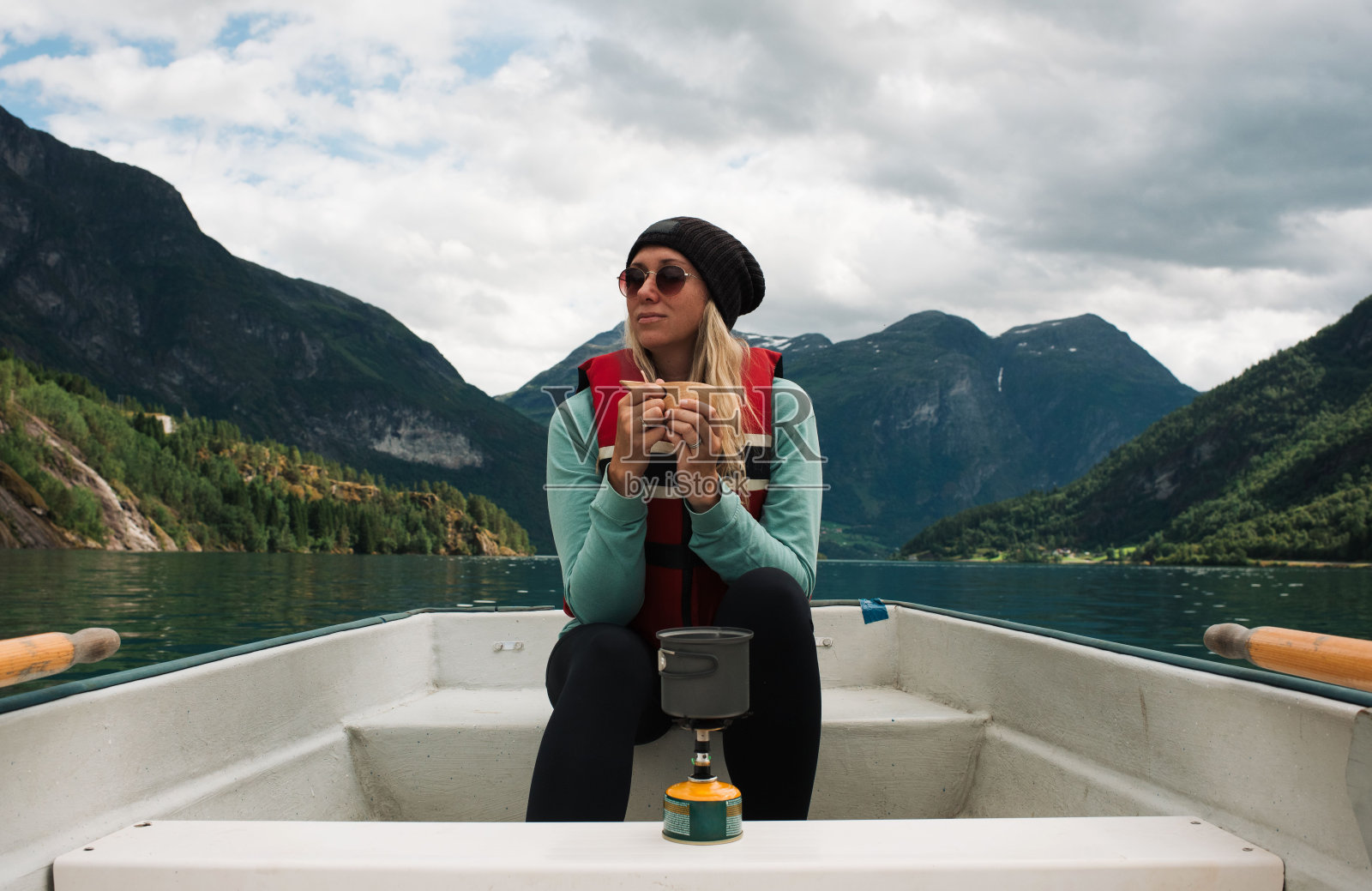 一位女士在挪威峡湾的独木舟上喝着热饮照片摄影图片