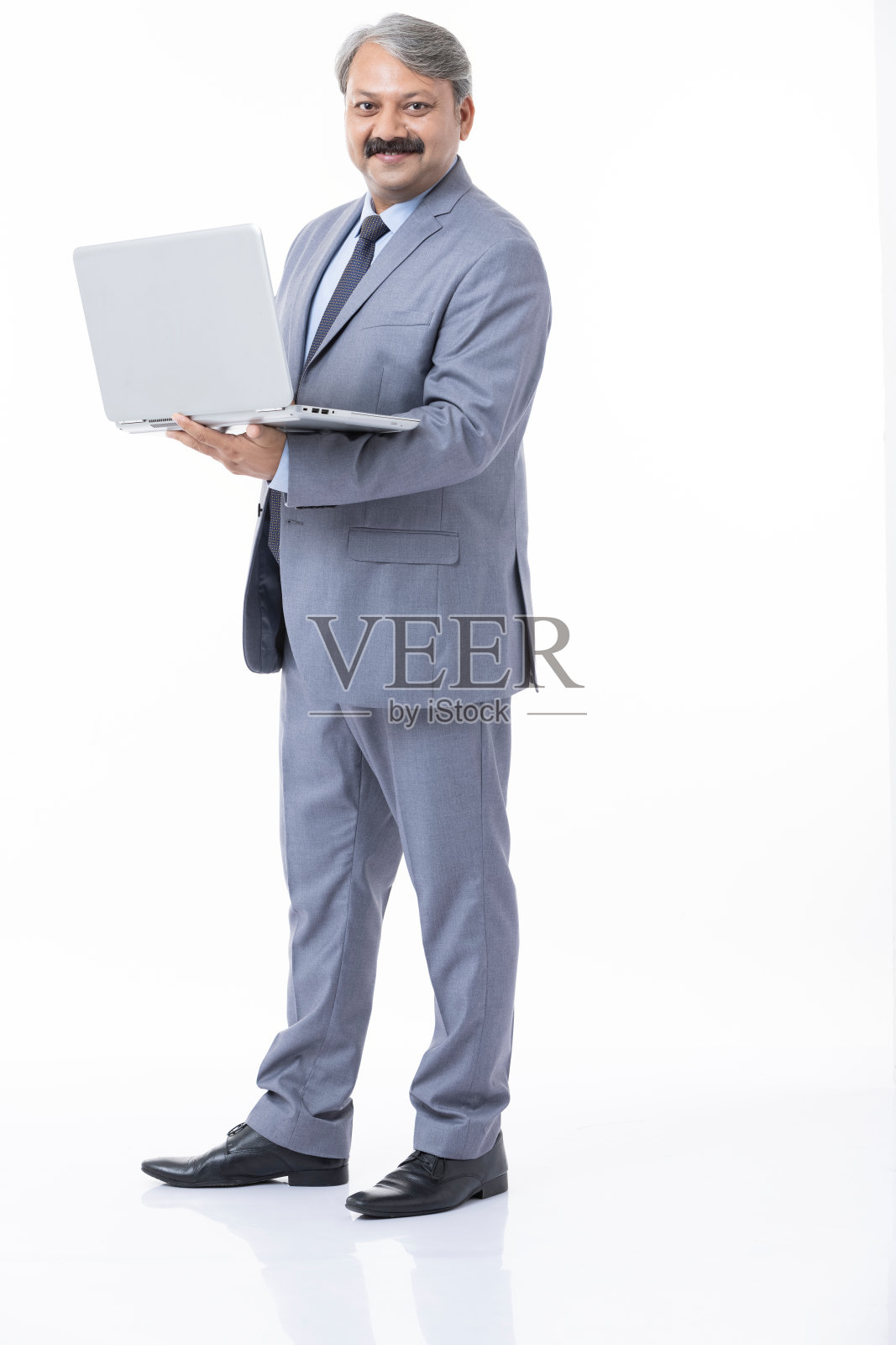 微笑英俊的年轻印度商人穿着西装拿着笔记本电脑孤立在白色背景。照片摄影图片