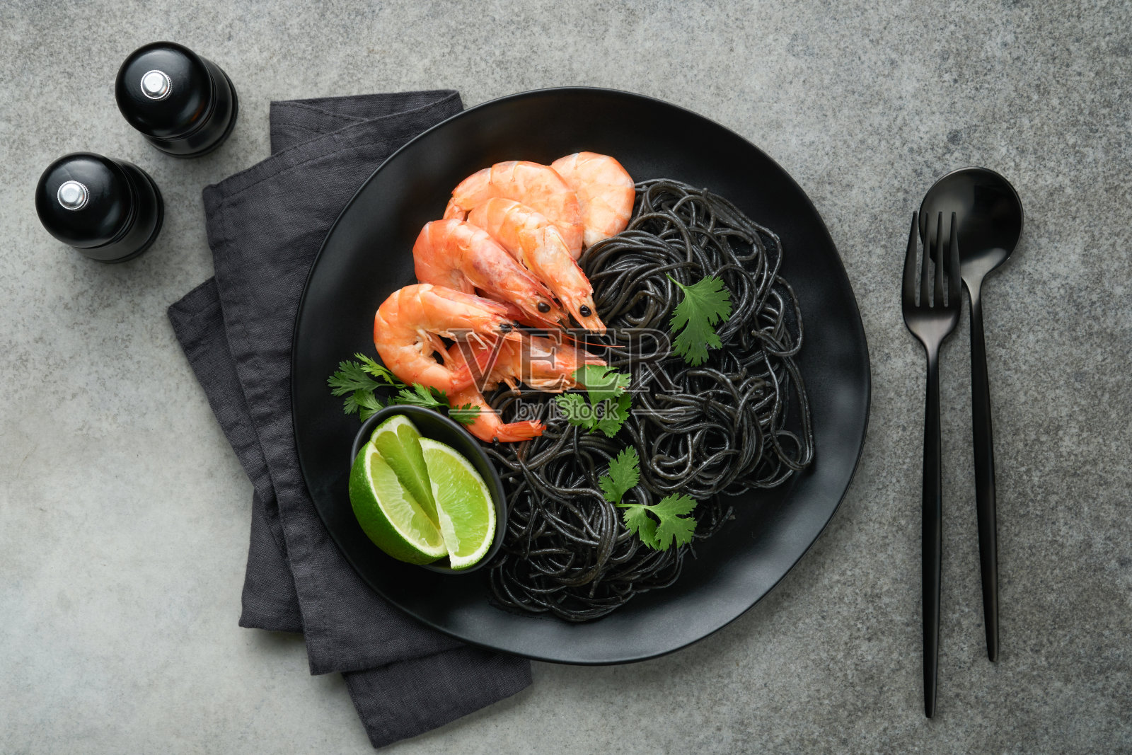 黑色的意大利面，意大利面虾在黑色的盘子上，黑色的混凝土桌子背景。鱿鱼墨对虾意面。意大利海鲜。灰色石桌的俯视图。地中海传统菜肴。照片摄影图片