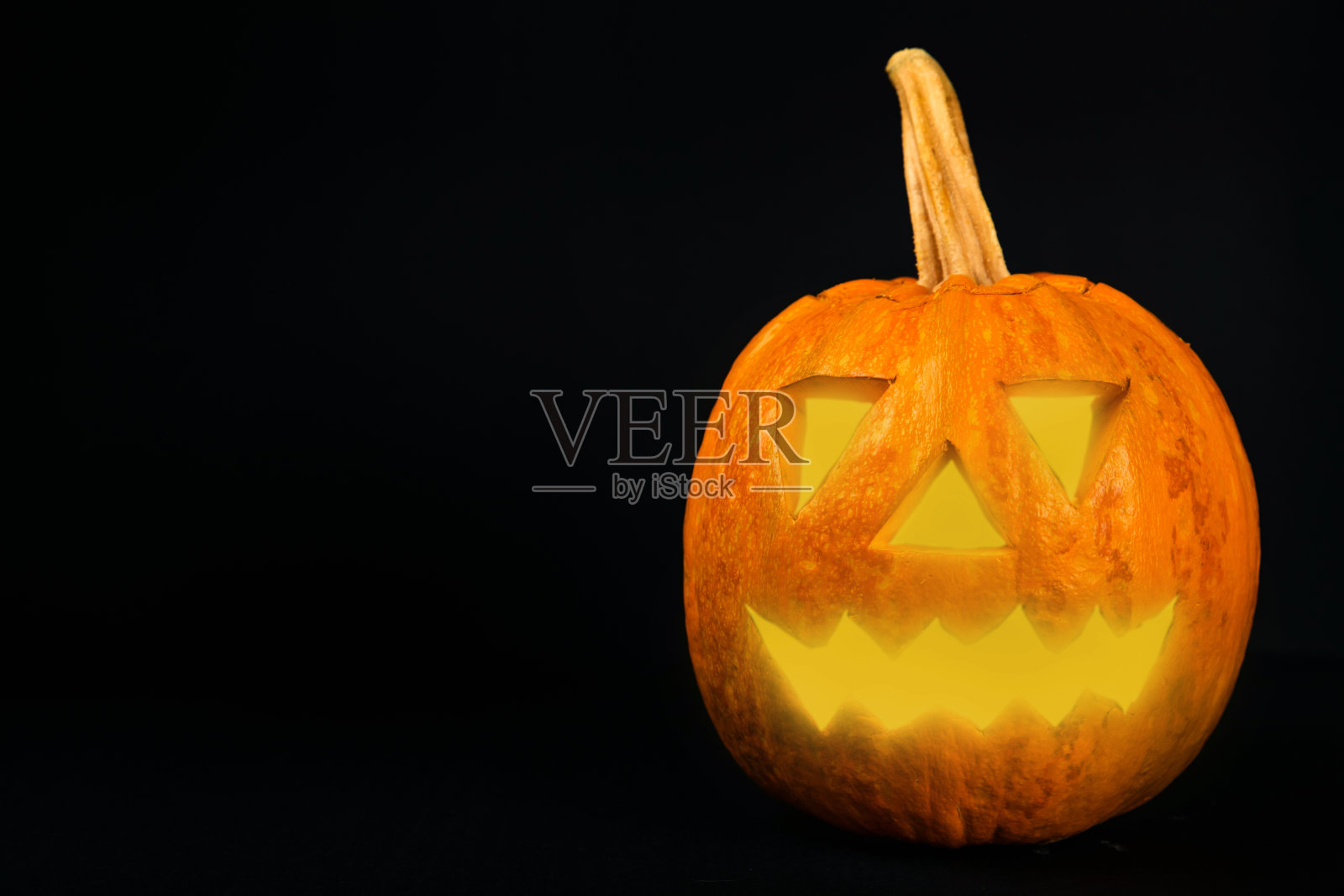 万圣节南瓜上有棕色的木质纹理。暗背景上的构图。可怕的构图与发光的眼睛和嘴。节日的概念。本空间照片摄影图片