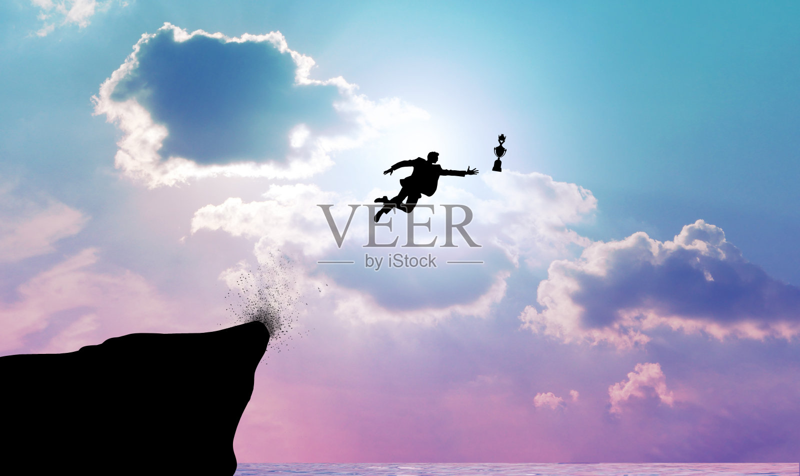 一个商人为了战利品从悬崖上跳下来的剪影。商业概念的决策，勇气和冒险的成功。照片摄影图片