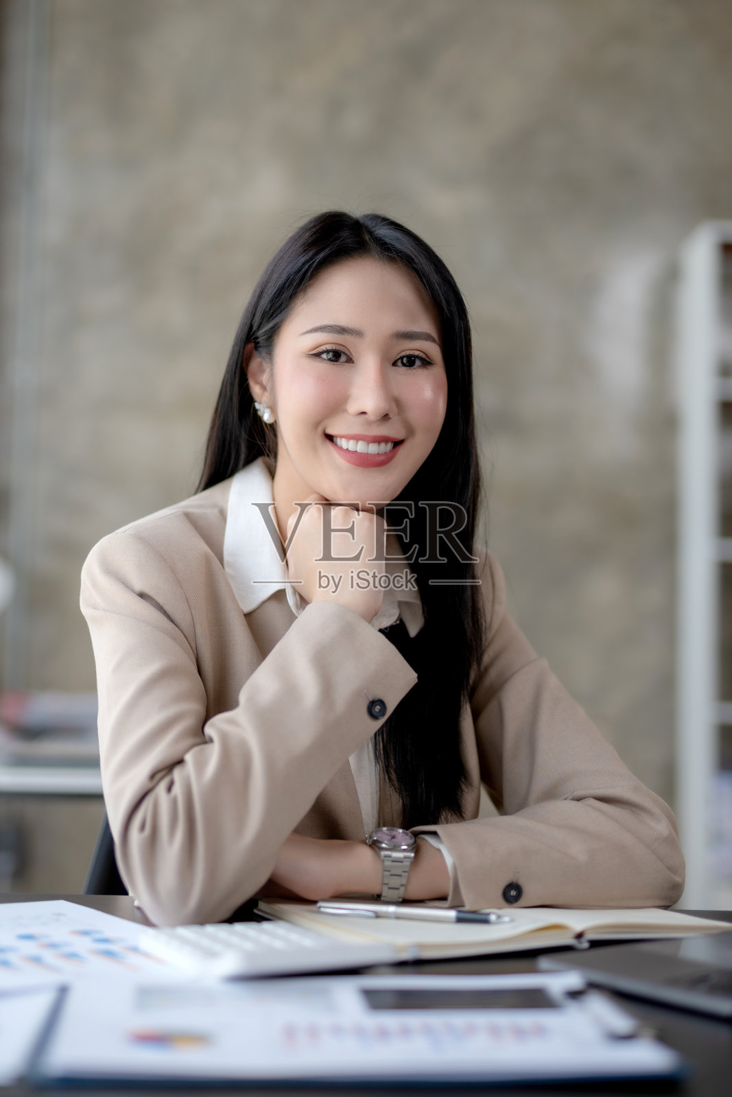 美丽的亚洲女商人坐在办公室里，对着镜头微笑，开心地工作。照片摄影图片