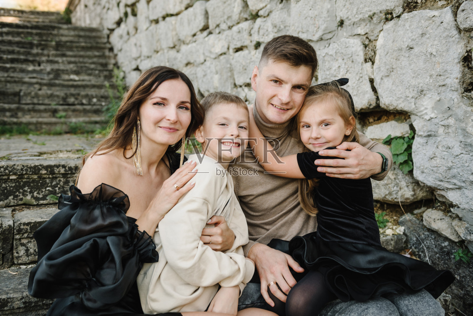 孩子们在老砖墙旁拥抱父母。日落时分，母亲、父亲、女儿、儿子坐在古代宫殿附近的楼梯上。妈妈，爸爸在大自然中拥抱快乐的孩子们。家人聚在一起。特写镜头照片摄影图片
