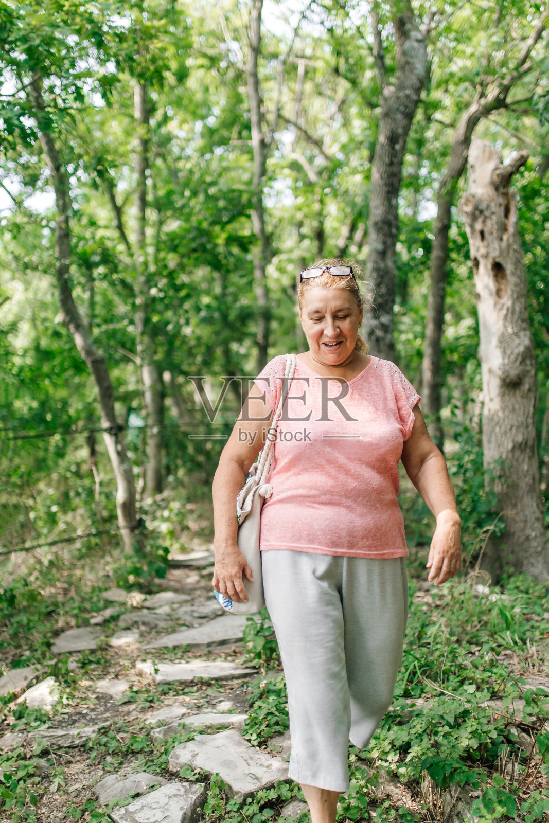 欣喜的成年女子独自走下石径，看着脚在苍翠的野林中。兴致勃勃的游客沿着危险的路线行走。登山、主动娱乐、度假照片摄影图片